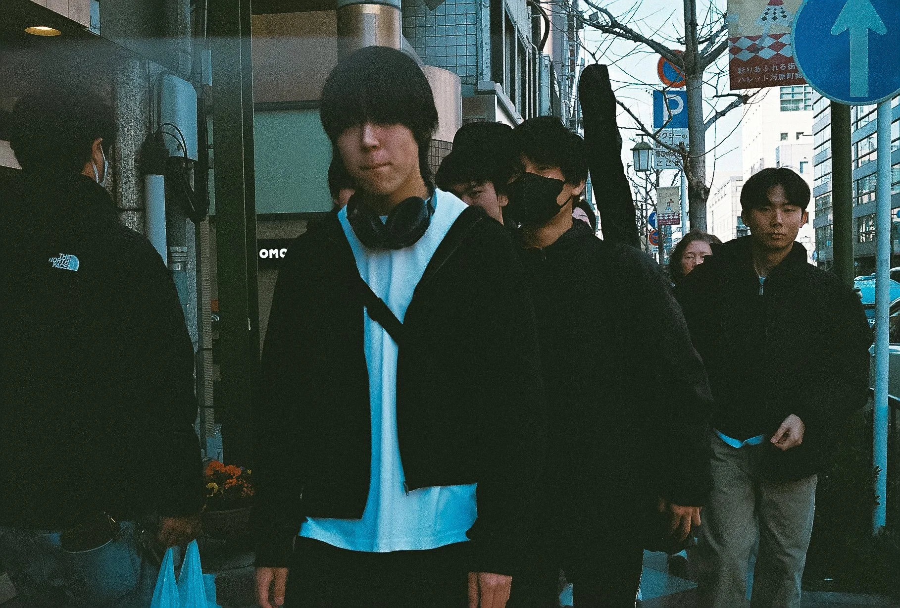 Candid street portrait of a young man walking down a bustling Japanese city street.