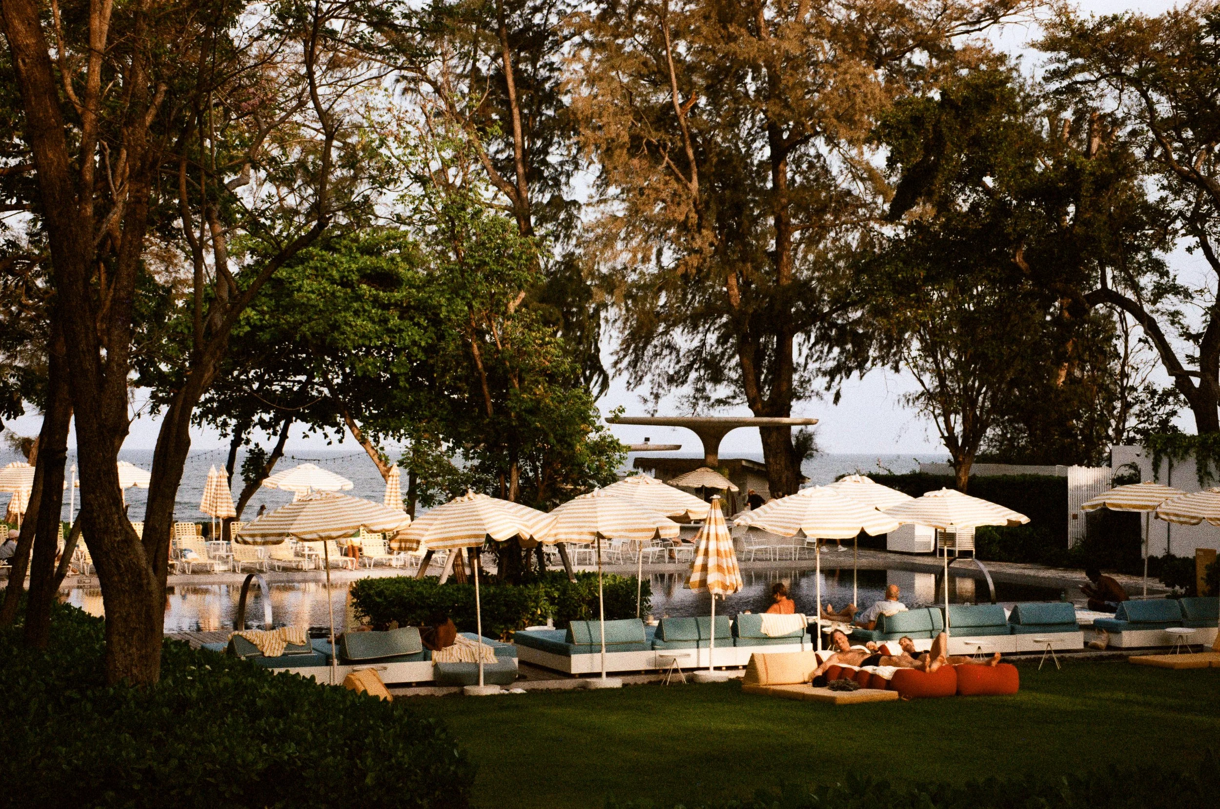 A tropical resort beach view with umbrellas and lush green trees in Hua Hin, Thailand.