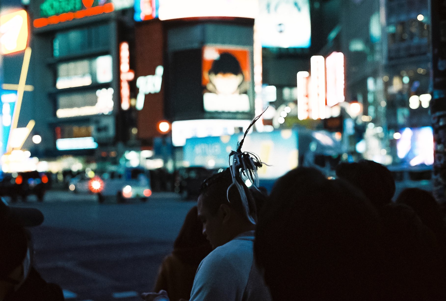 Crowd of people crossing a busy Japanese street illuminated by bright neon shop signs at night.