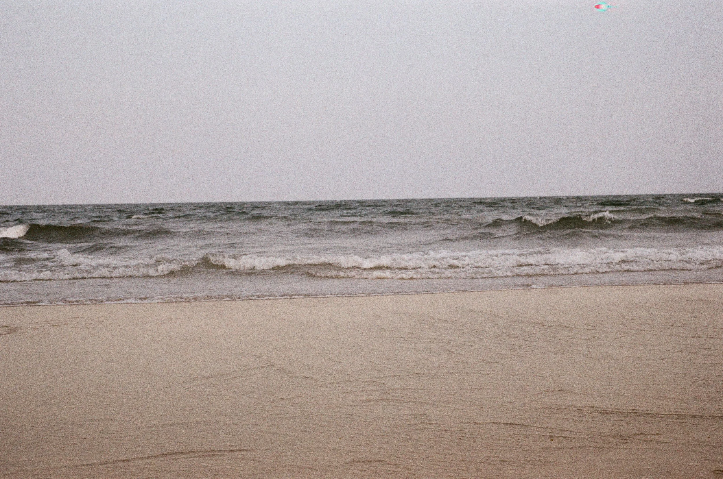 Minimalist film photography of gentle ocean waves rolling onto a sandy beach in Thailand.