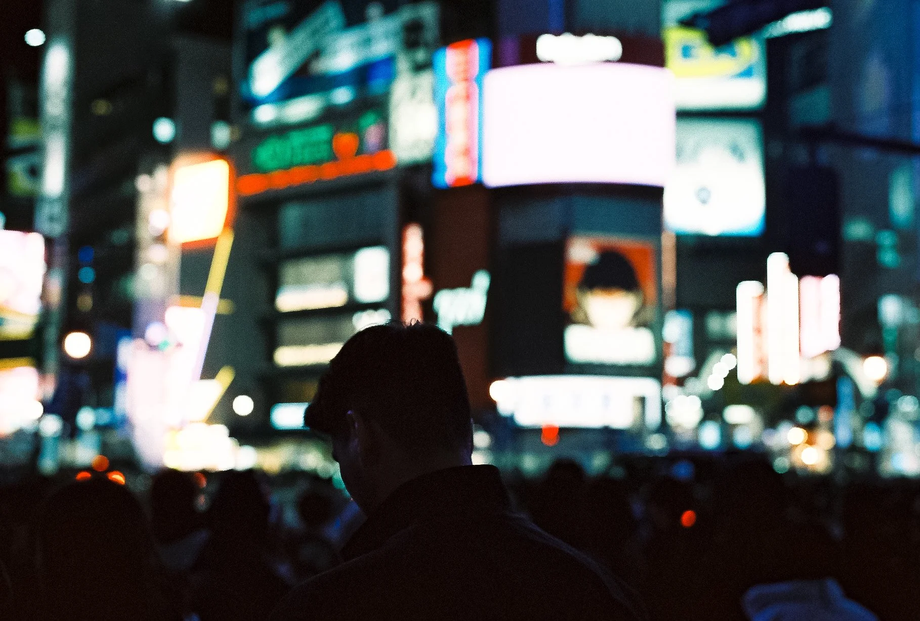 Dark silhouette of a person standing against brightly blurred neon billboards in Tokyo at night.