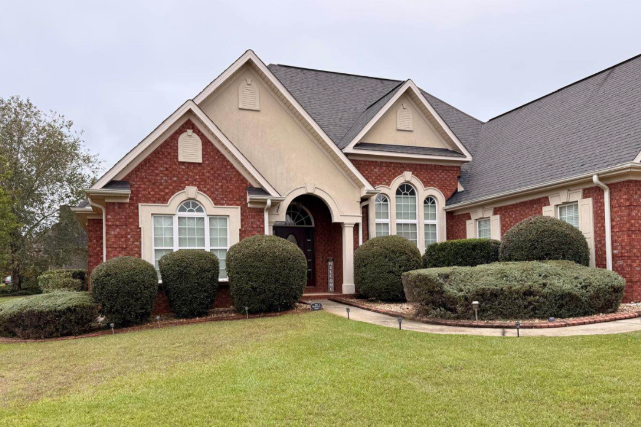 A large brick house with a manicured front yard, rounded bushes, and multiple arched windows.