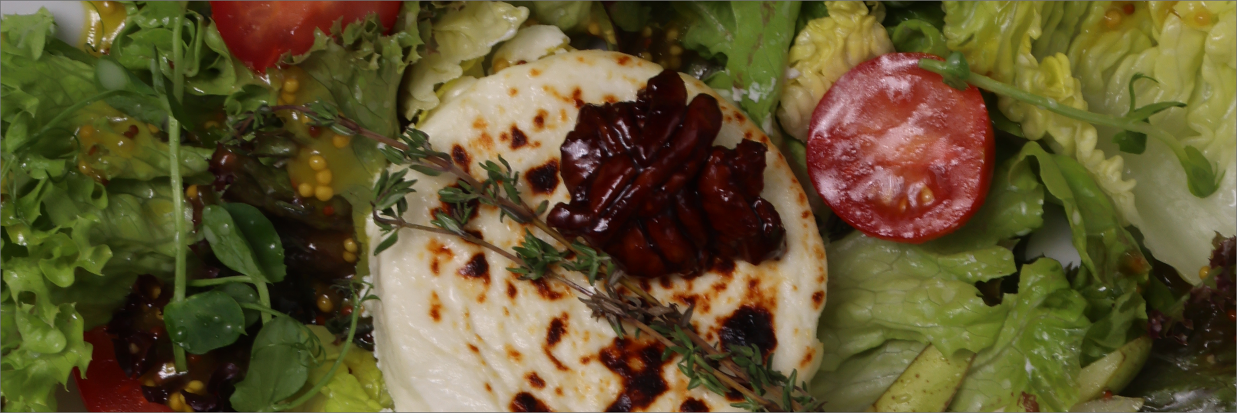Close-up of a fresh salad with leafy greens, cherry tomatoes, grilled cheese with a topping, and fresh herbs.