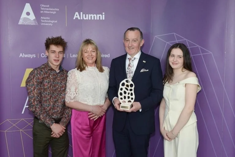 Daniel, Maria, Michael & Ciallann standing on a purple stage backdrop with the Atlantic Technological University logo and 'Alumni' text. Michael holds a trophy, and the others stand beside him, smiling.