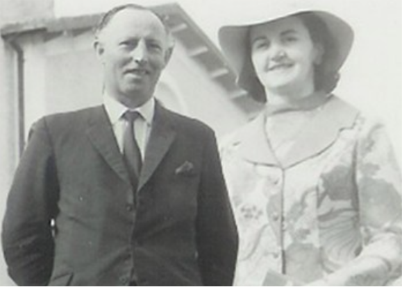 A black and white photo of Michael & Phil Vaughan outdoors, both dressed in formal attire, standing close together and smiling.