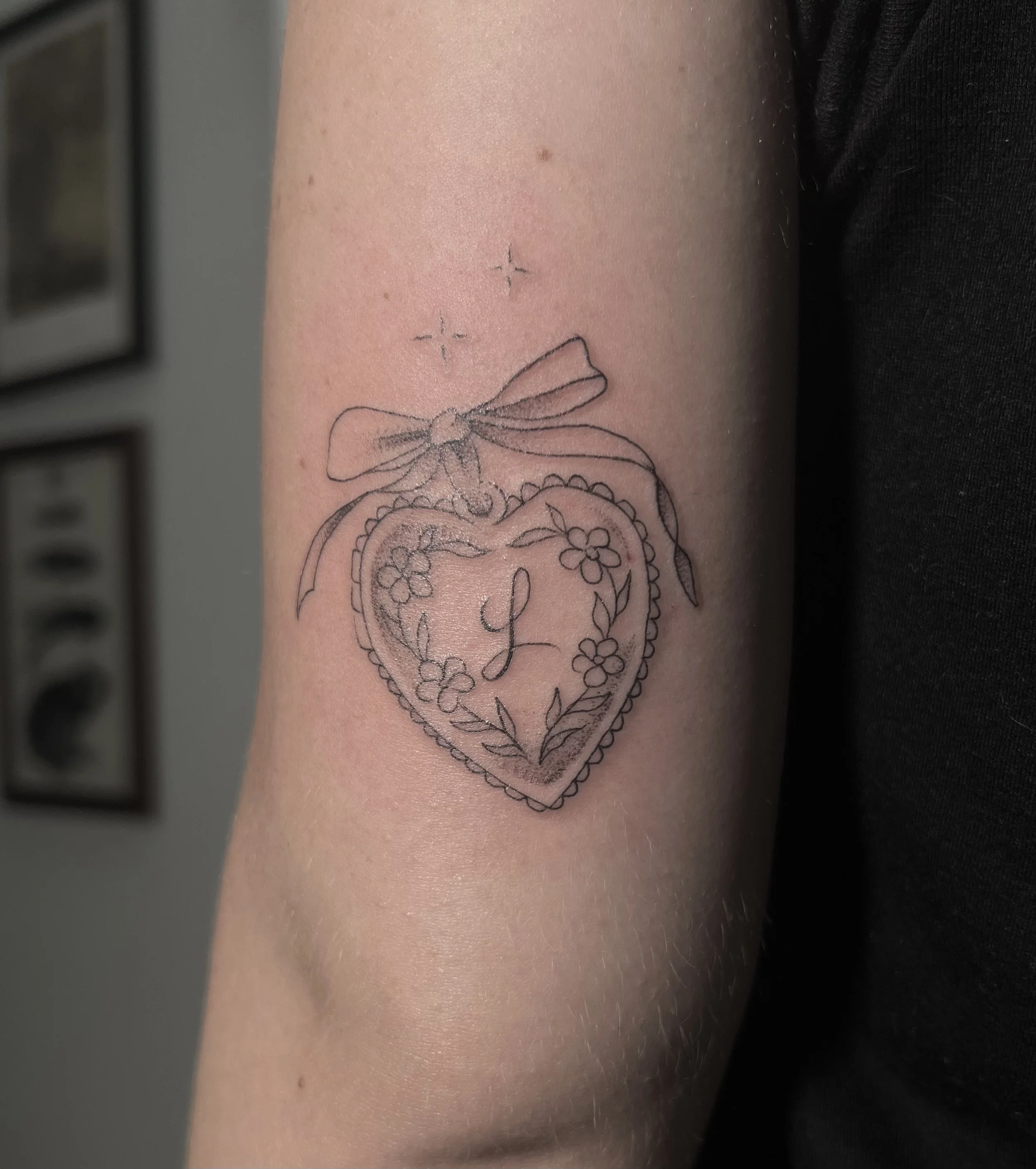 Tattoo of a heart with flowers and a bow on inner forearm.