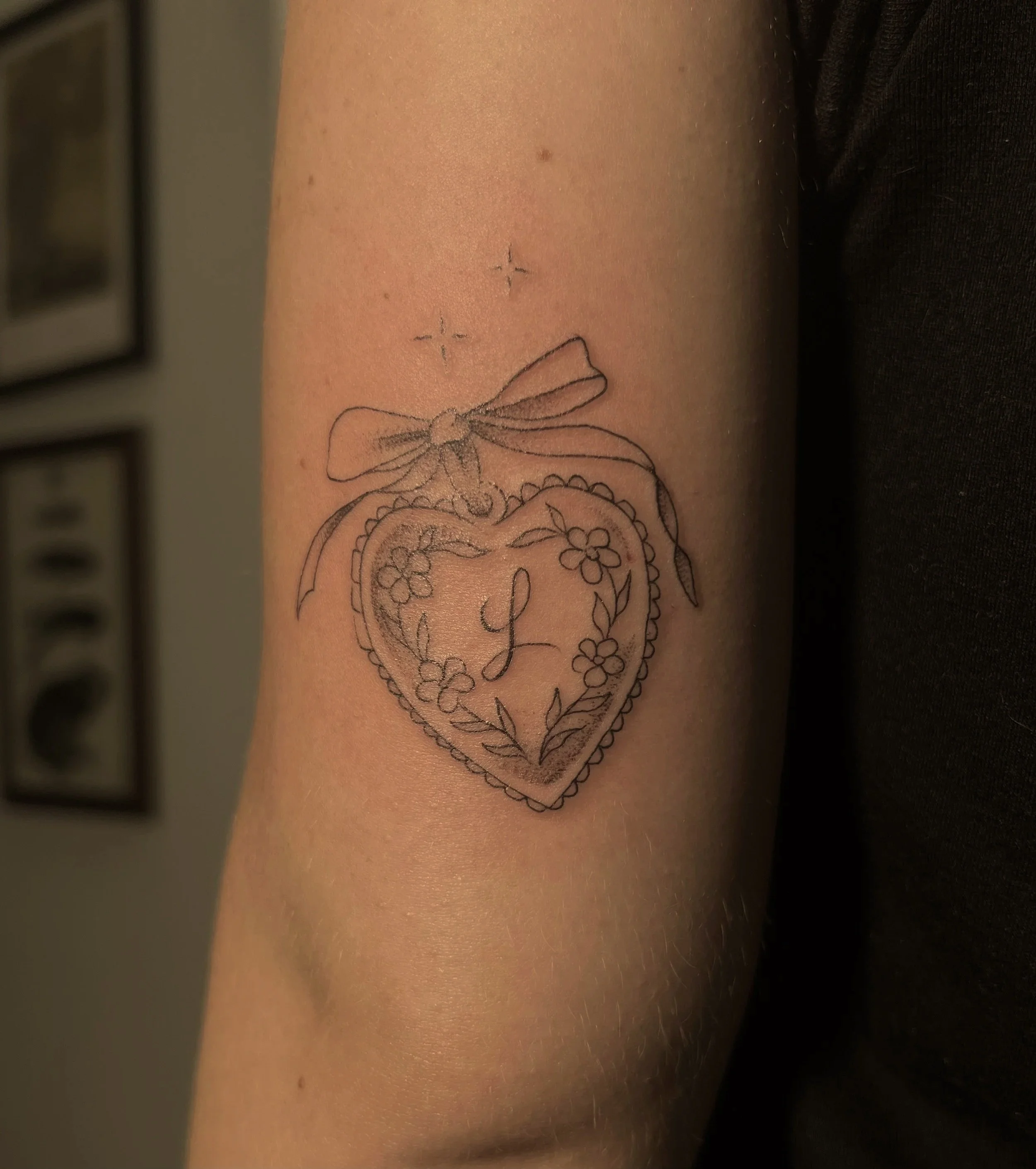 A tattoo of a heart with floral designs and a bow on a person's upper arm.