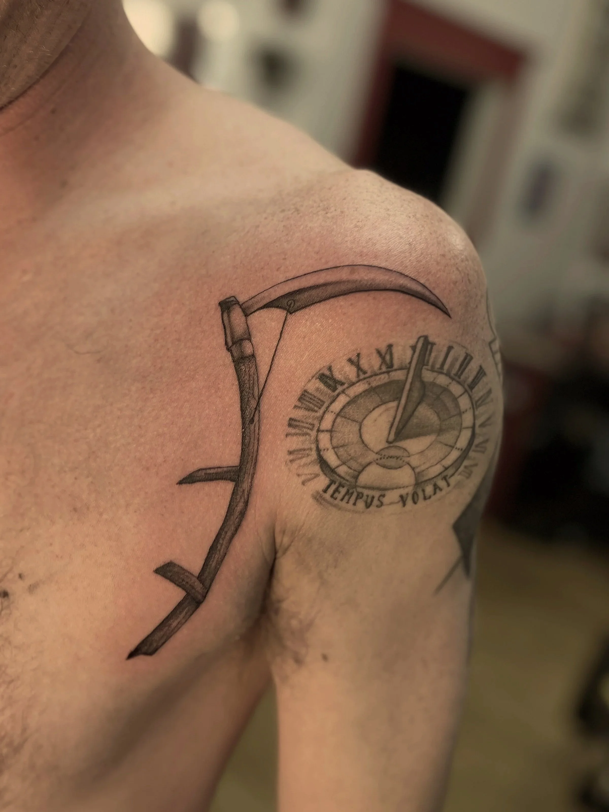 Close-up of a shoulder tattoo featuring a clock with Roman numerals and a banner with the Latin phrase 'Tempus Volat'.