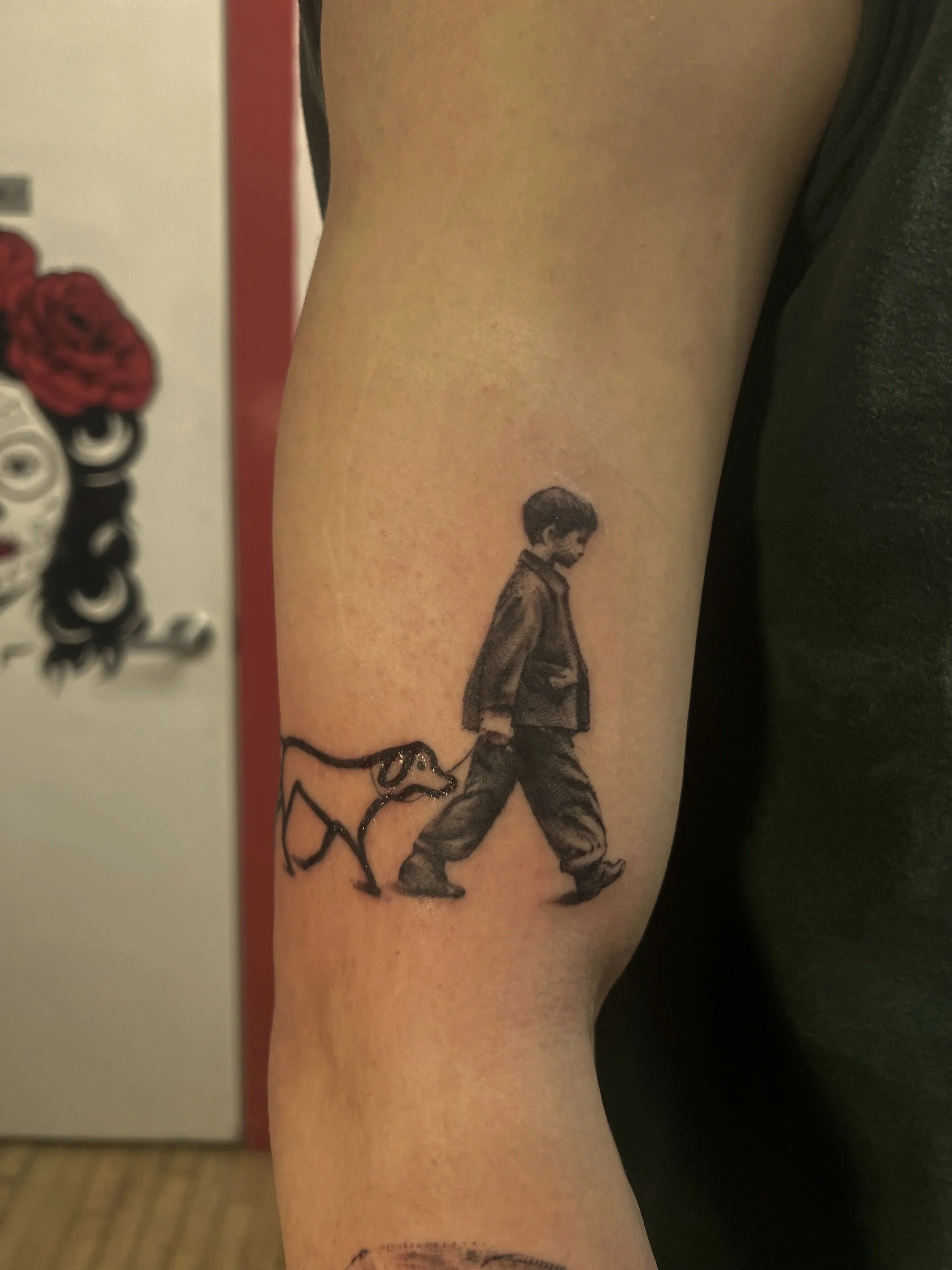 Tattoo of a young boy walking a dog on the person's arm.