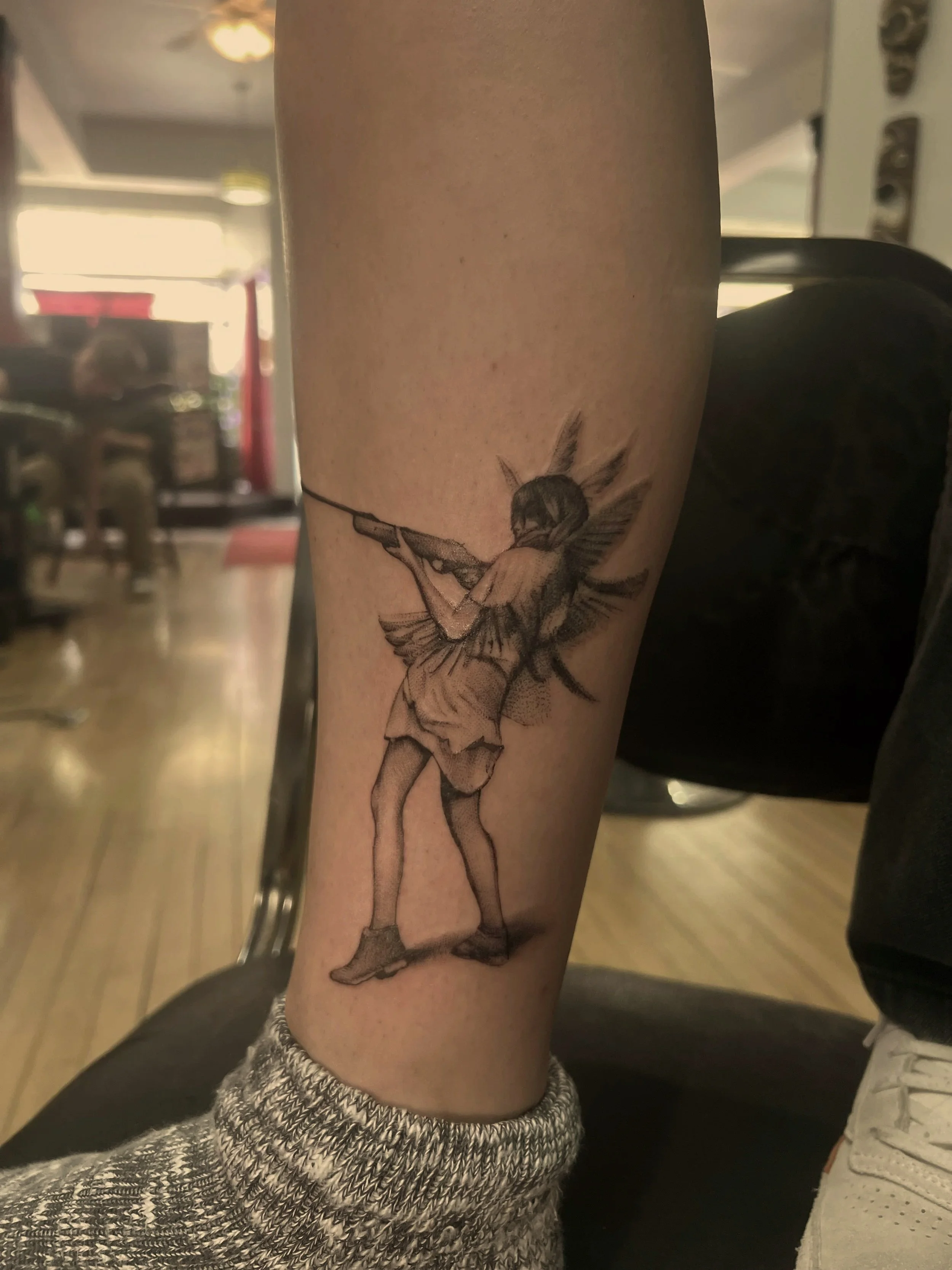 Tattoo of a ballerina girl with fairy wings holding a violin on a person's forearm.