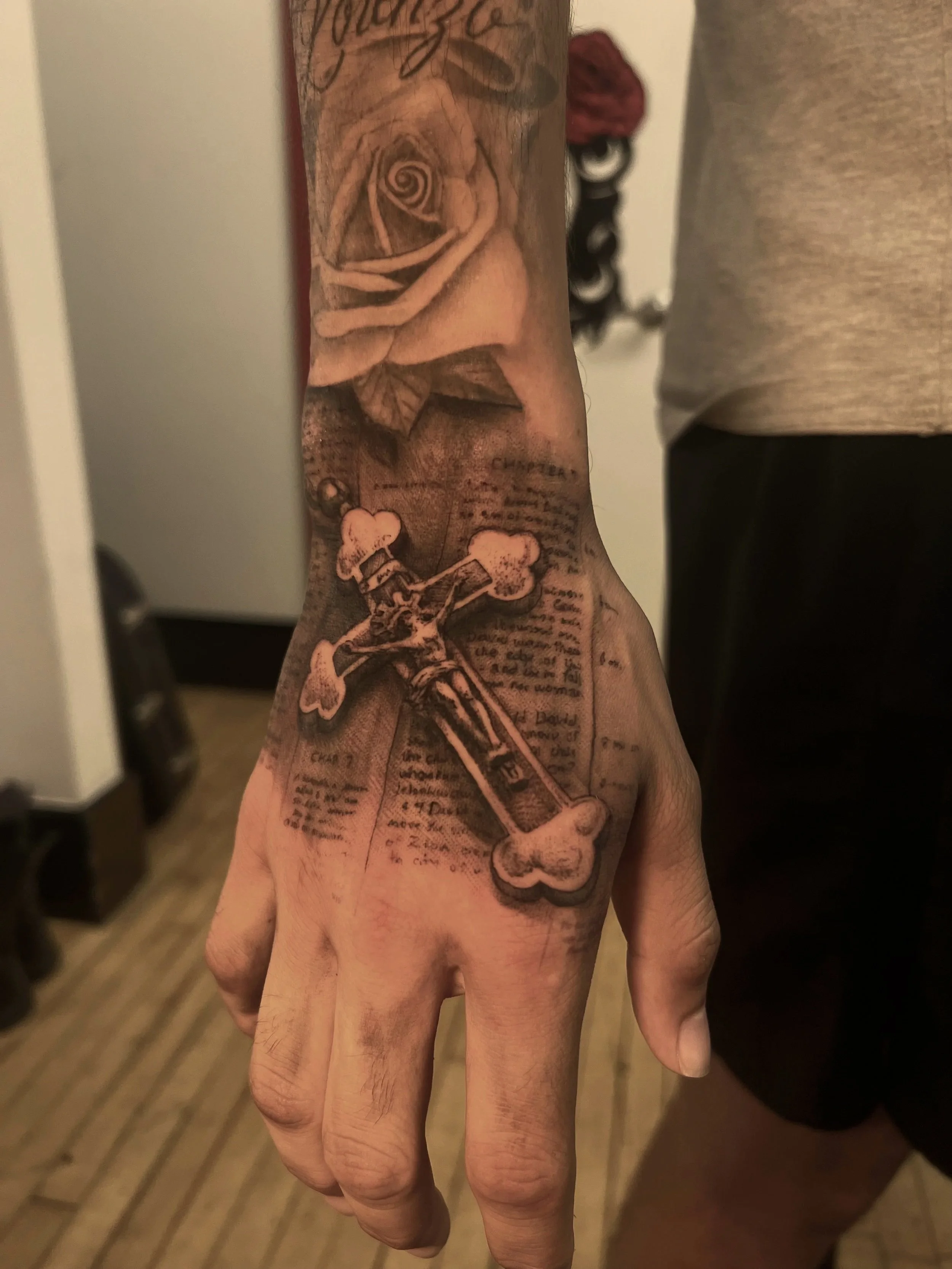 A detailed tattoo on a person's forearm depicting a rose, a skeleton playing a guitar, and handwritten text.