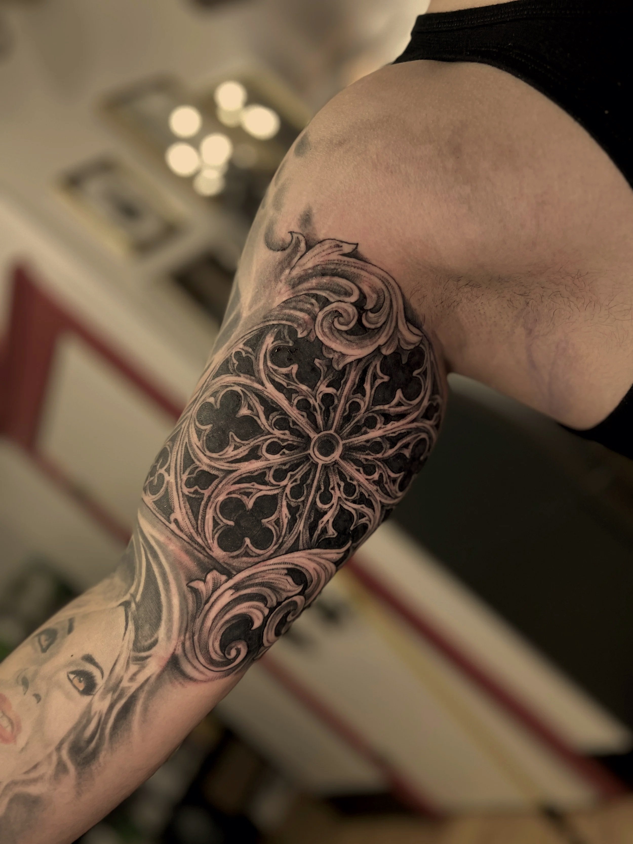Close-up of a person's arm with an elaborate black and gray tattoo sleeve featuring floral and geometric patterns.