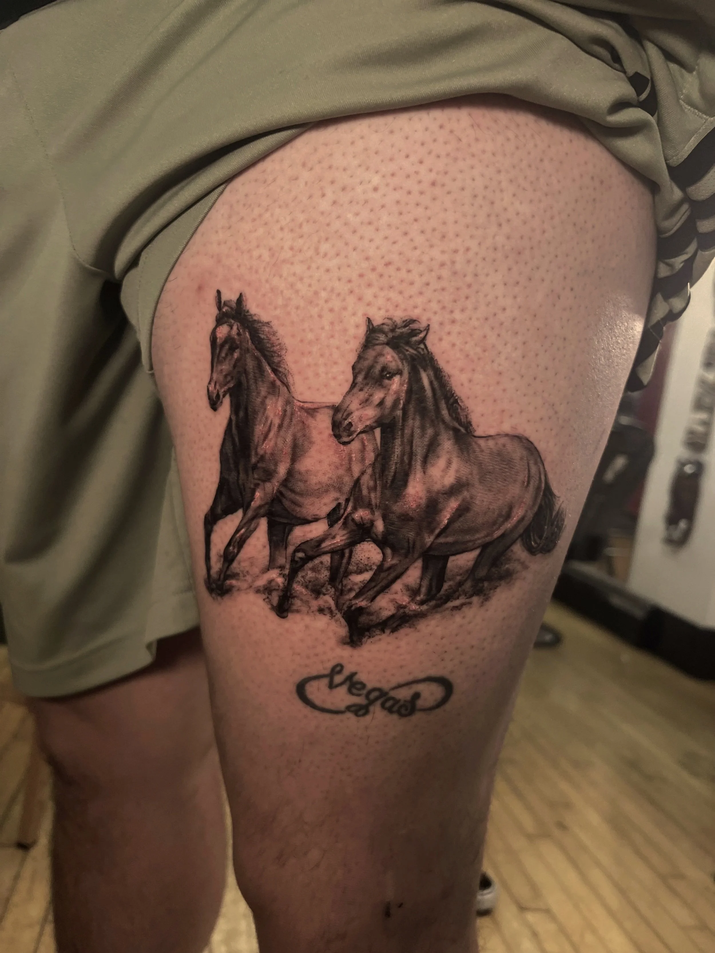 Close-up of a person's upper thigh with a tattoo of two horses and a 'Vegan' logo beneath it.