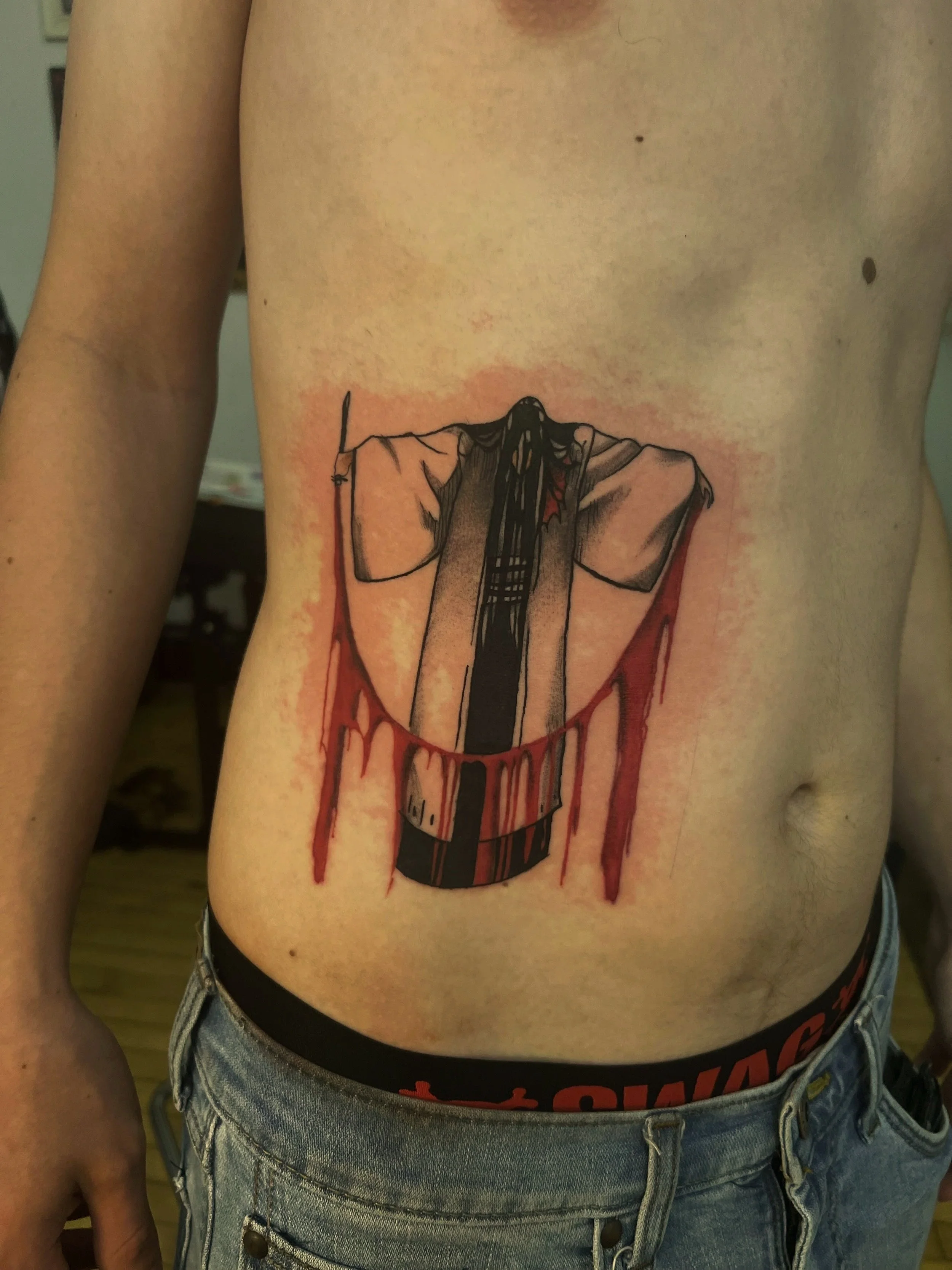 Tattoo on a person's side waist of a figure with wings, holding a sword in front of them, with red ink dripping down. Anime reference from Bleach