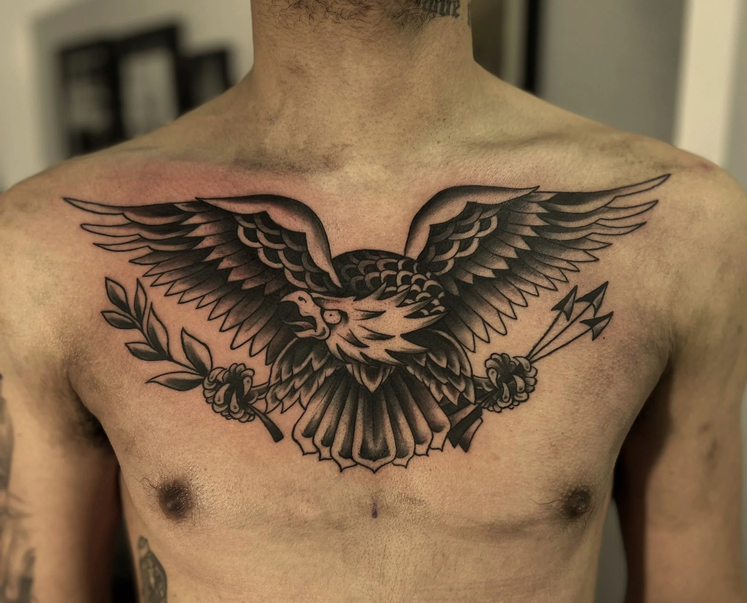 Close-up of a person's chest with a black and gray tattoo of a bird with wings spread wide.