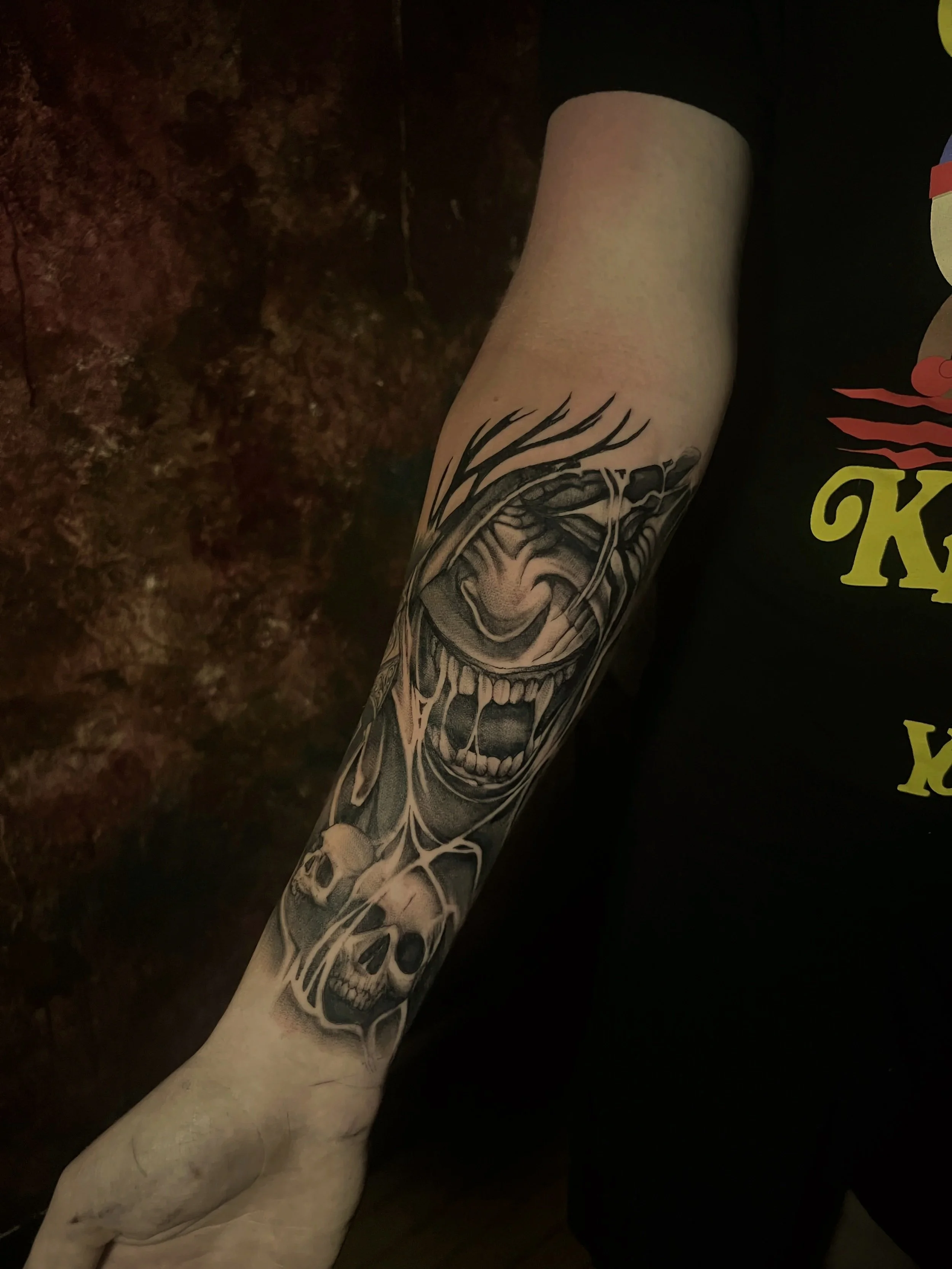 Black and white tattoo of a skull with a wide smile and sharp teeth on a person's arm.