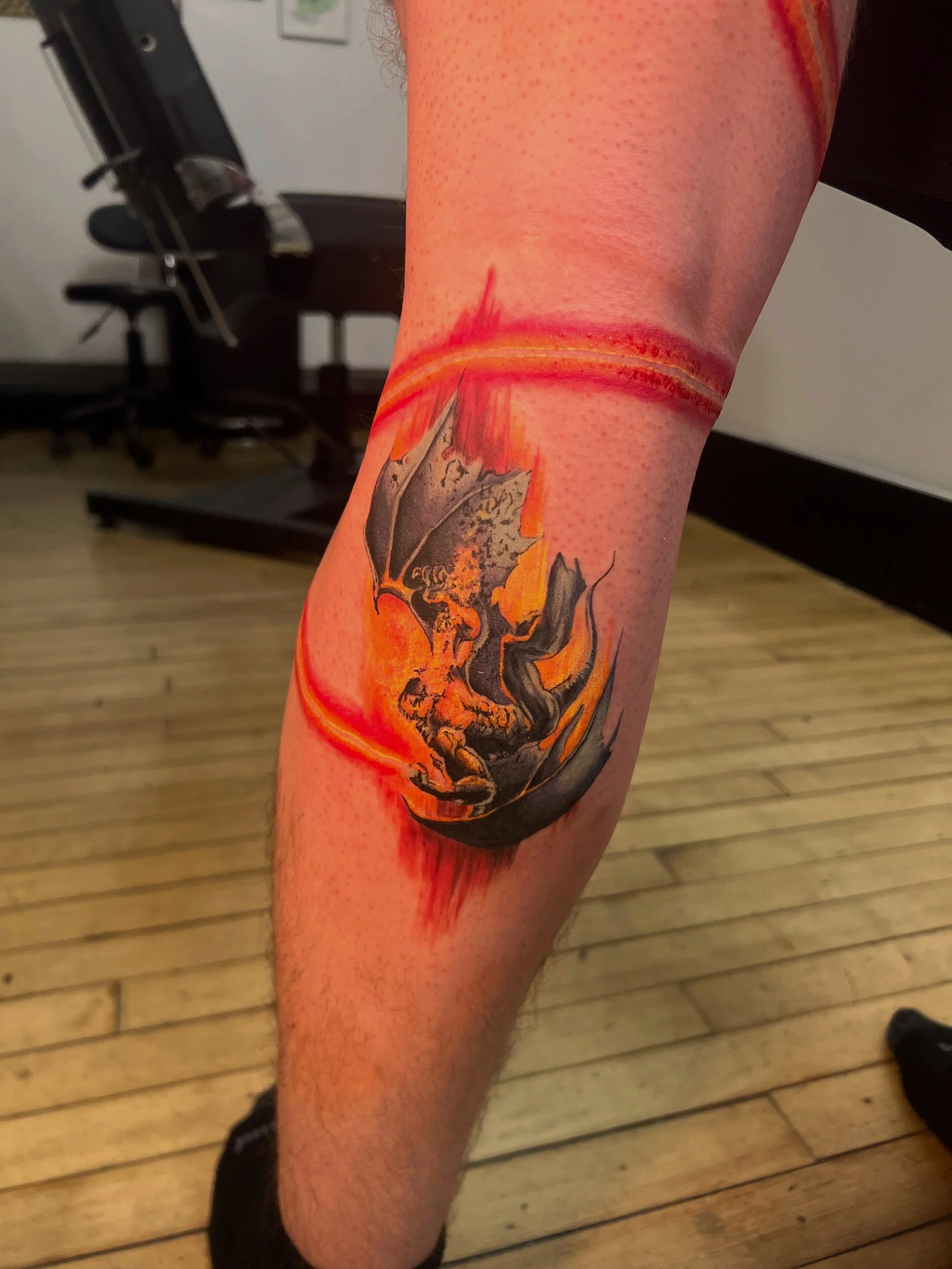 A tattoo of a black dragon and a fiery background on a person's leg. From a lord of the rings tattoo