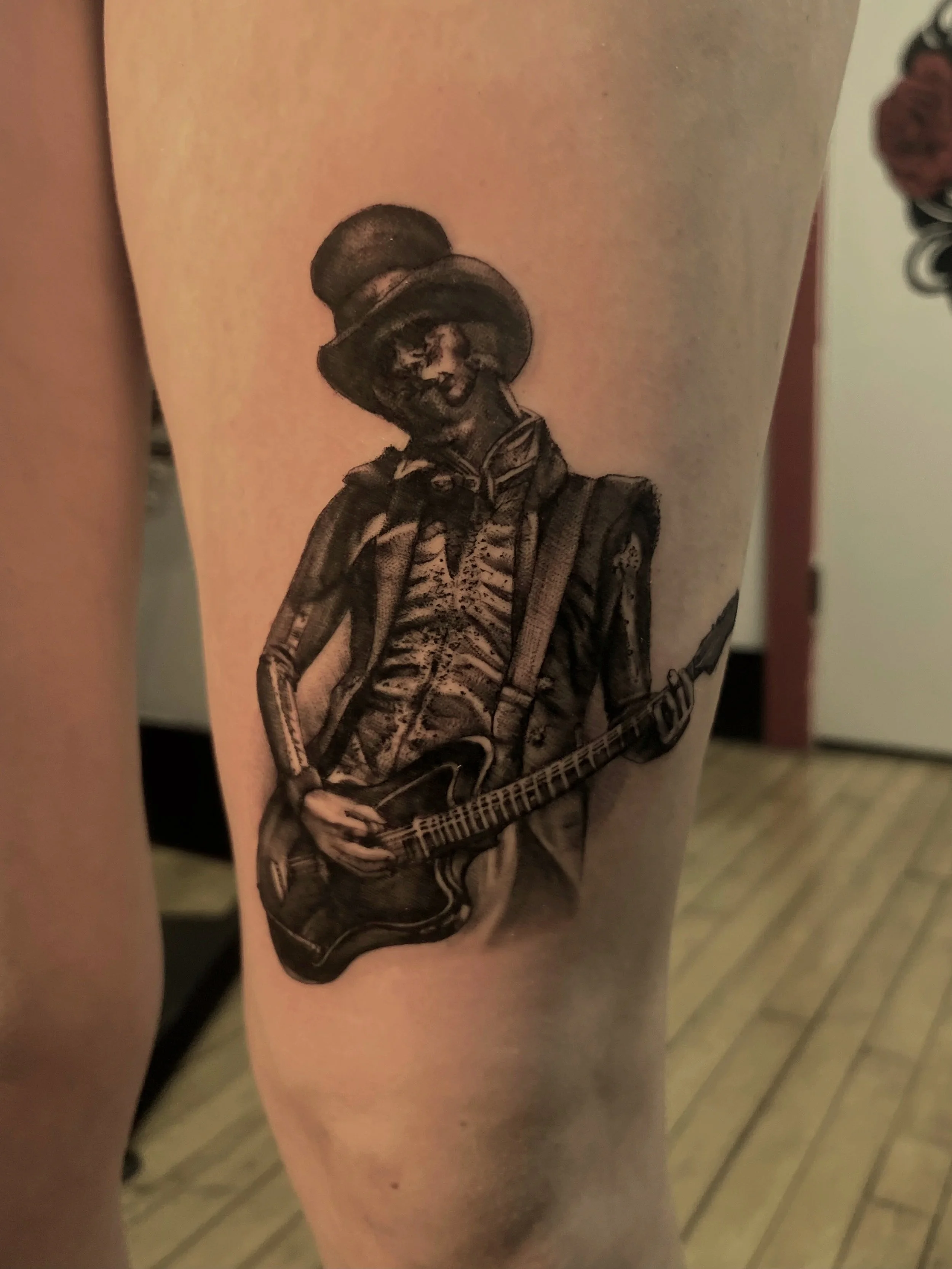 Tattoo of a person wearing a top hat and playing an electric guitar on a person's arm. From the band Ghost