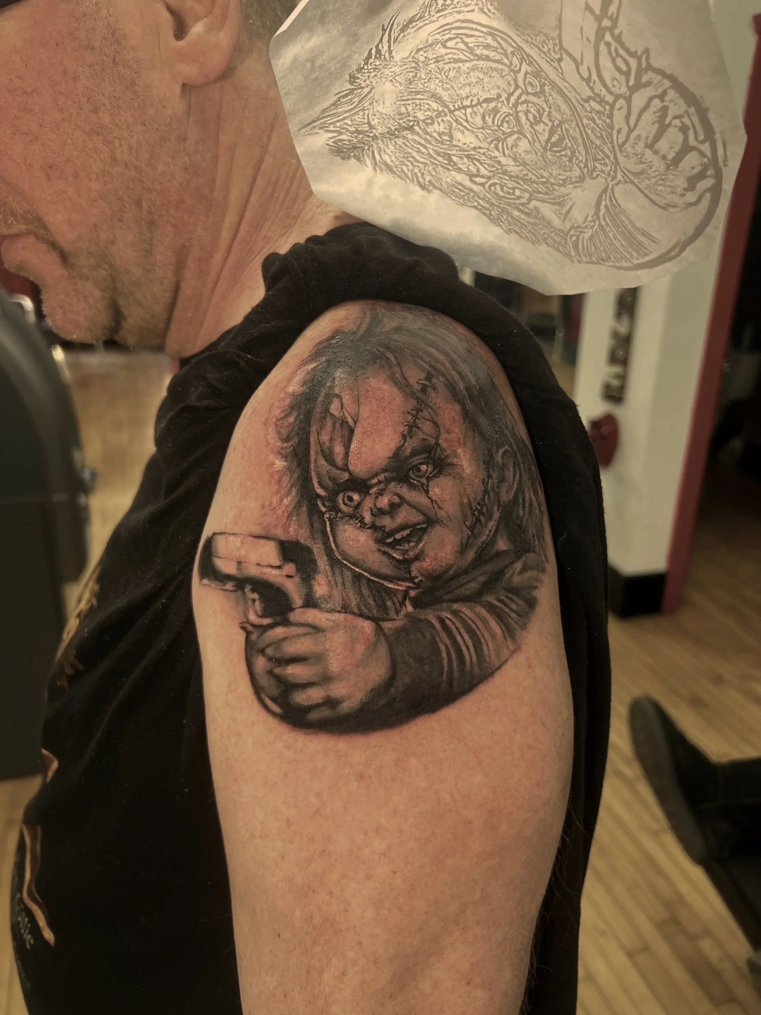 A tattoo of Chucky from the Chunky movies on person's upper arm.