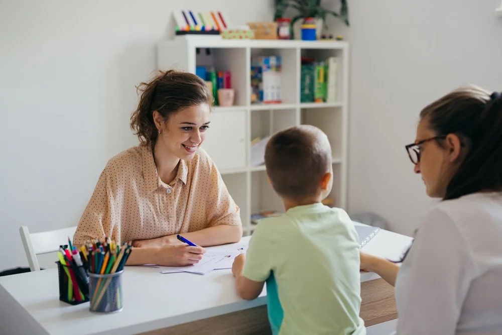 A woman and a healthcare professional sitting at a table, talking to a young boy after being partnered through the Colorado Children's Alliance.