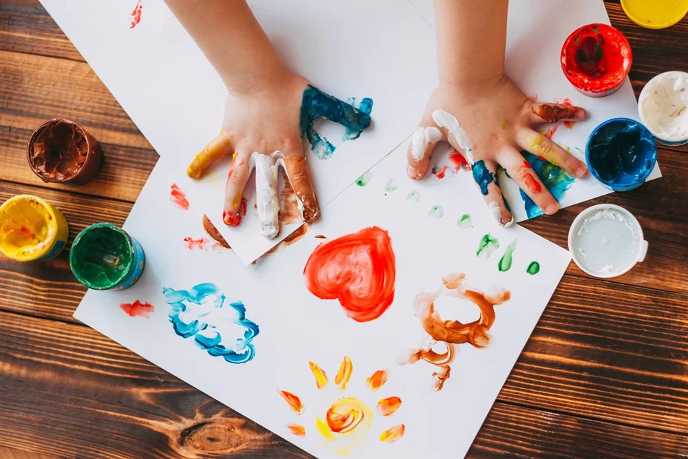 Child's hands covered in colorful paint on white paper representing the work of the Colorado Children's Alliance.