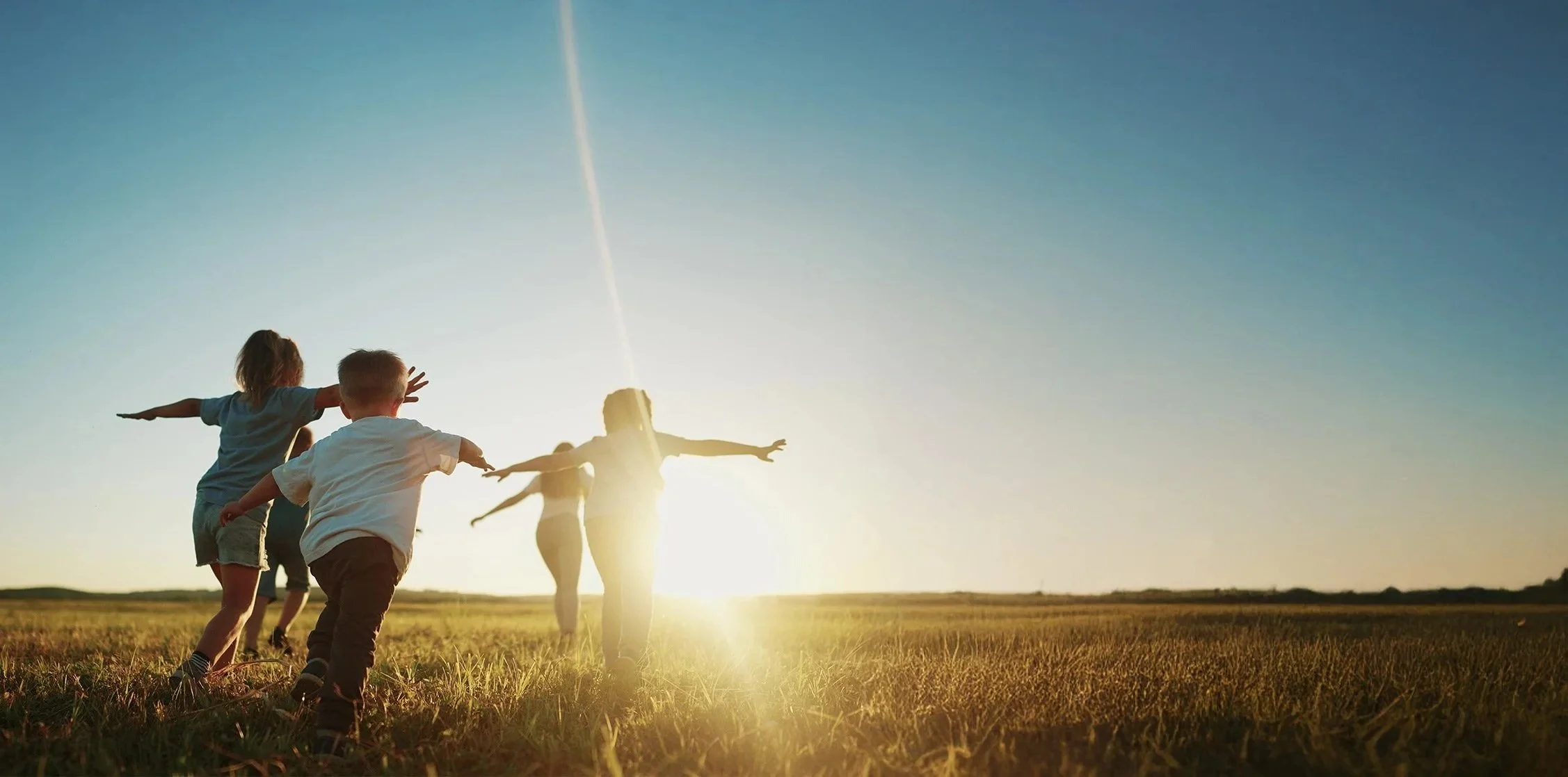Children running in a grassy field during sunset with arms outstretched to symbolize the impact made by the Colorado Children's Alliance.
