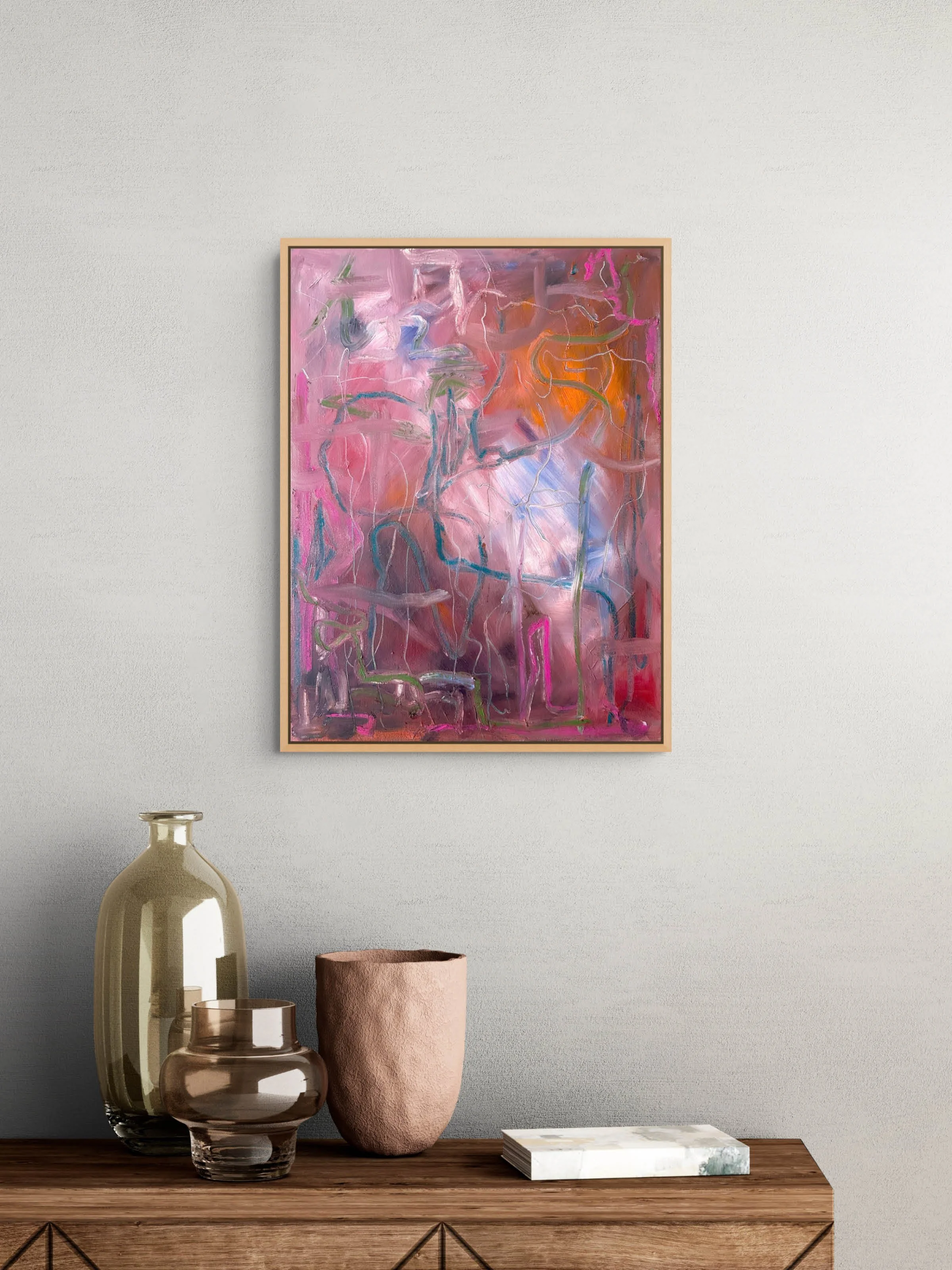 A wooden sideboard with decorative vases and a marble box, with an abstract pink and orange painting hanging on a white wall above.