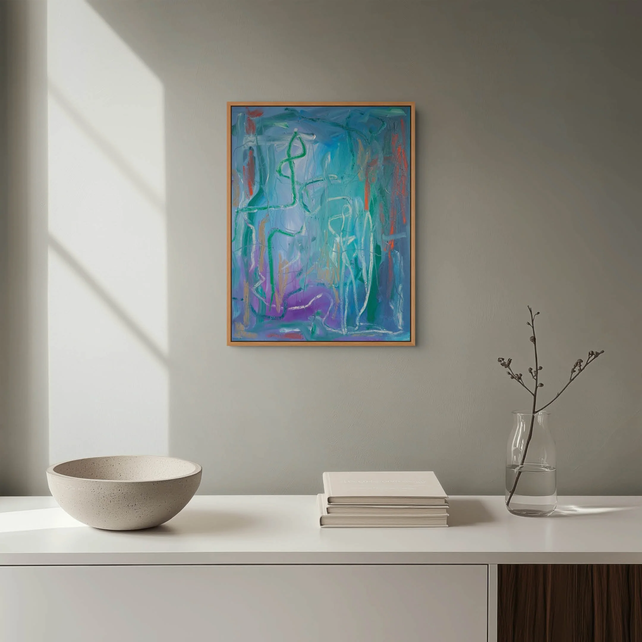 A white desk with minimalist decor, including a large abstract painting on the wall, a white bowl, a stack of books, and a clear vase with dried branches, illuminated by natural light.