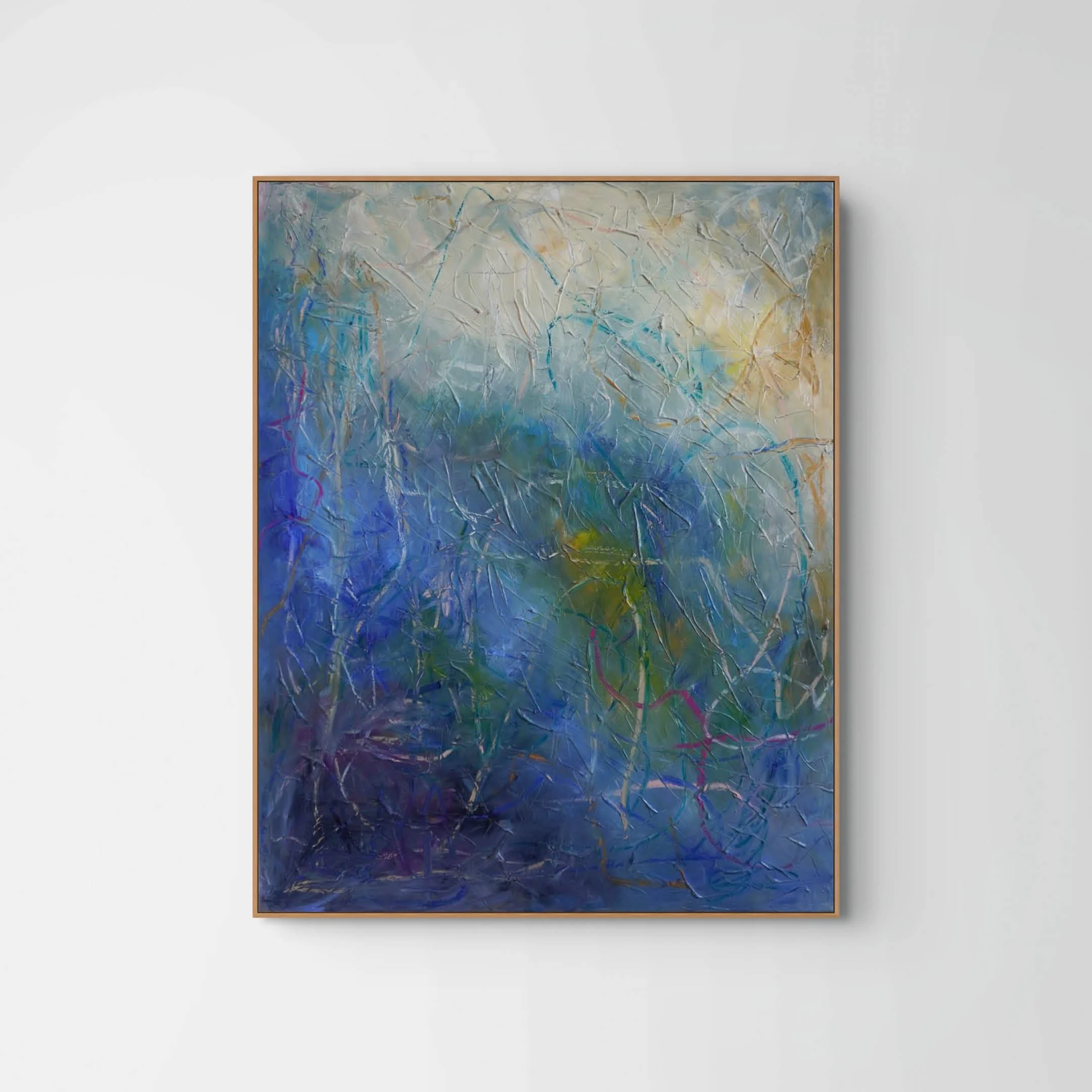 An abstract painting with swirling blue, white, yellow, and pink colors framed in light wood, displayed on a white wall.