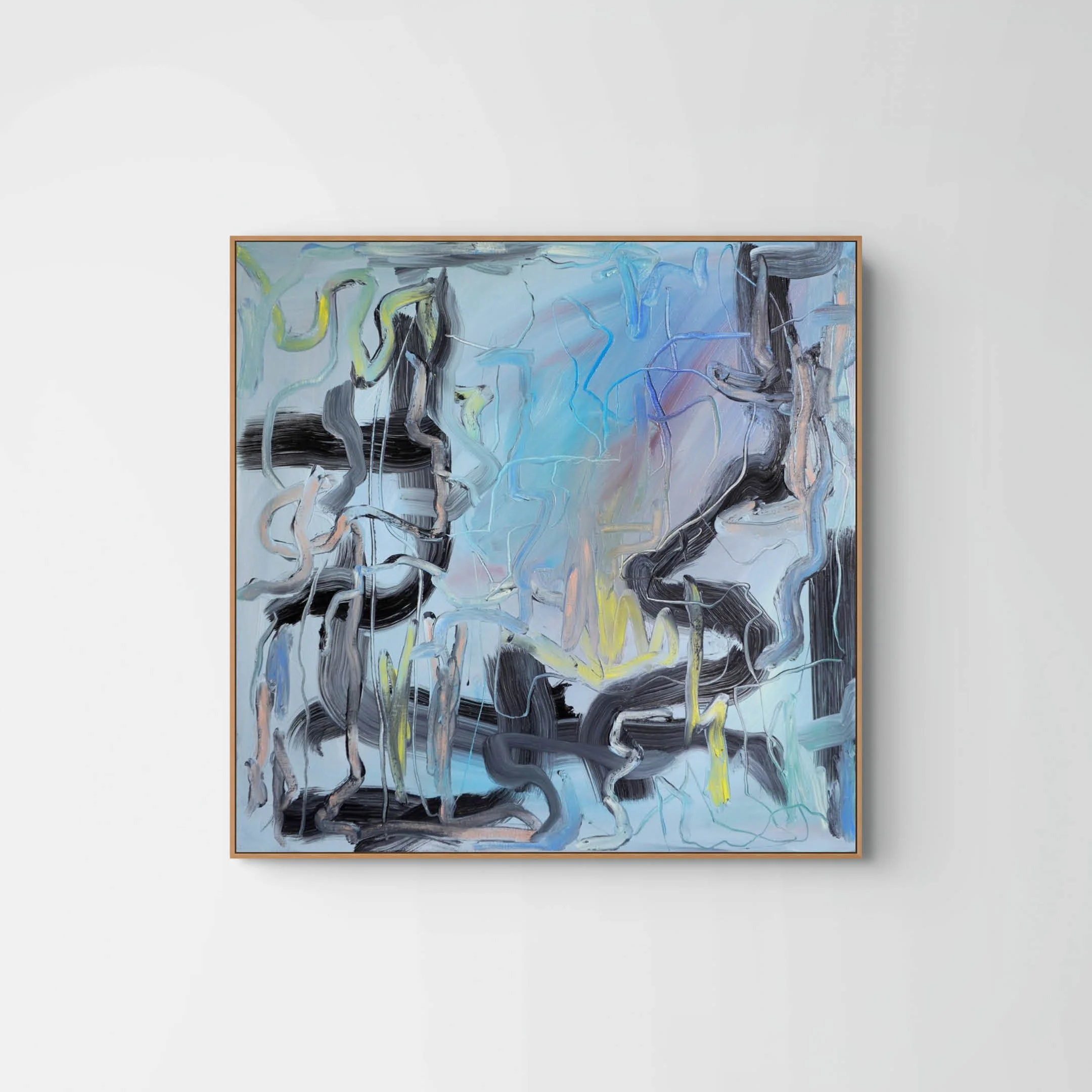 An abstract painting with swirling brushstrokes in shades of blue, black, gray, yellow, and hints of pink, framed in a light wood frame hanging on a plain white wall.
