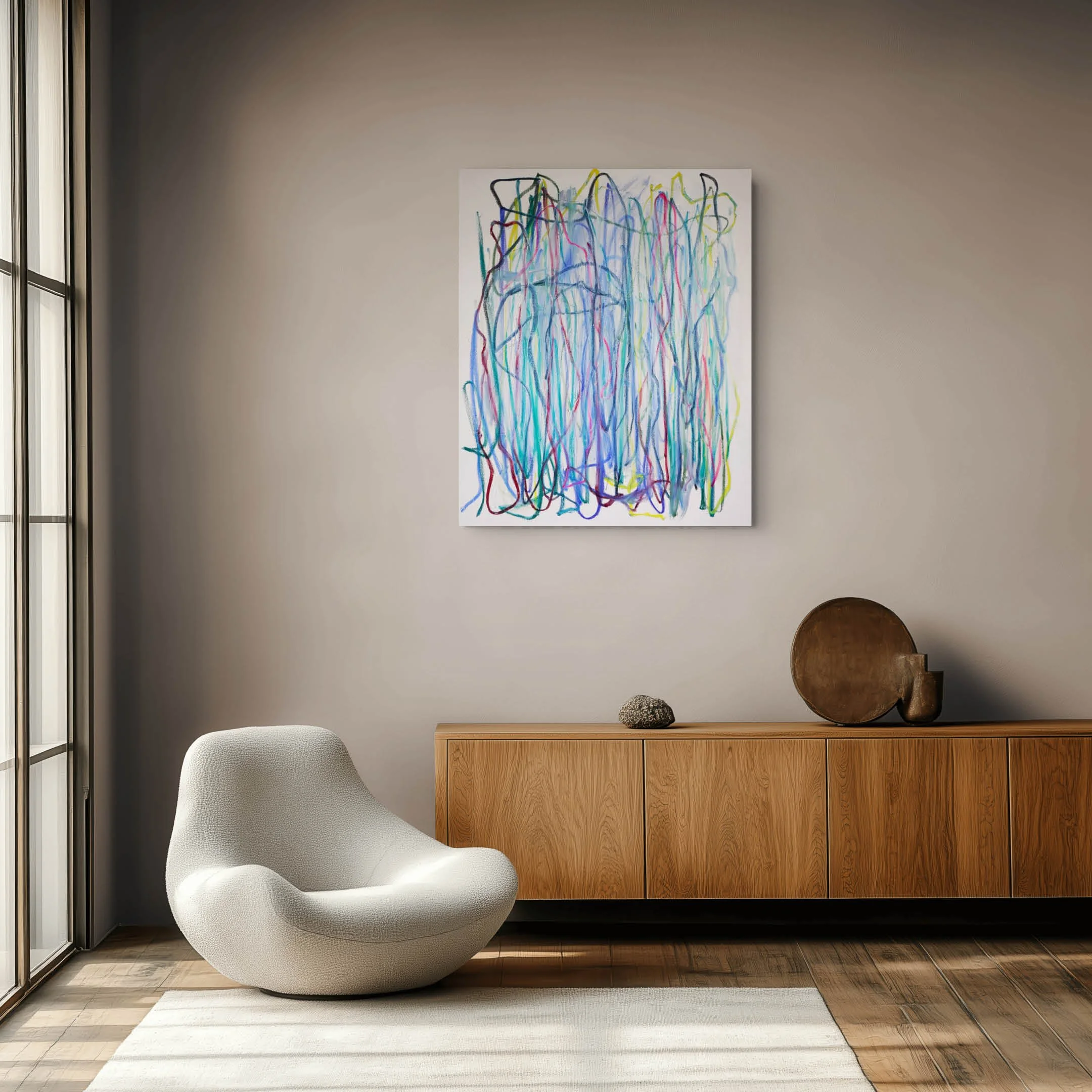 Modern living room corner with a white, plush armchair, a light wood cabinet, decorative objects, and abstract artwork on the wall. Natural light streams in from a large window.