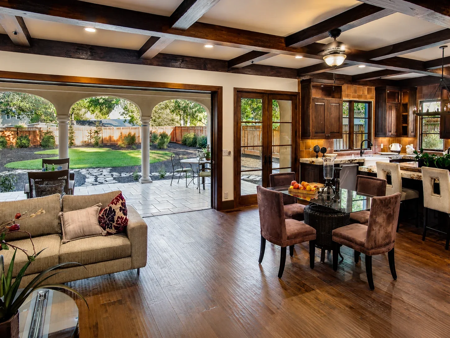 Kitchen and dining area at Villa Englewood in Los Gatos featuring dark wood cabinetry, a marble countertop, velvet dining chairs, and views to the backyard patio and landscaped lawn.
