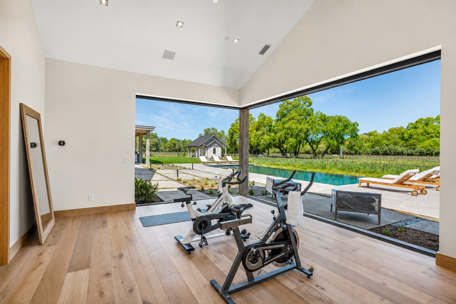 Wellness room at Trubody Ranch in Napa Valley featuring indoor cycling equipment, mirrored walls, and views to the pool and landscaped grounds.