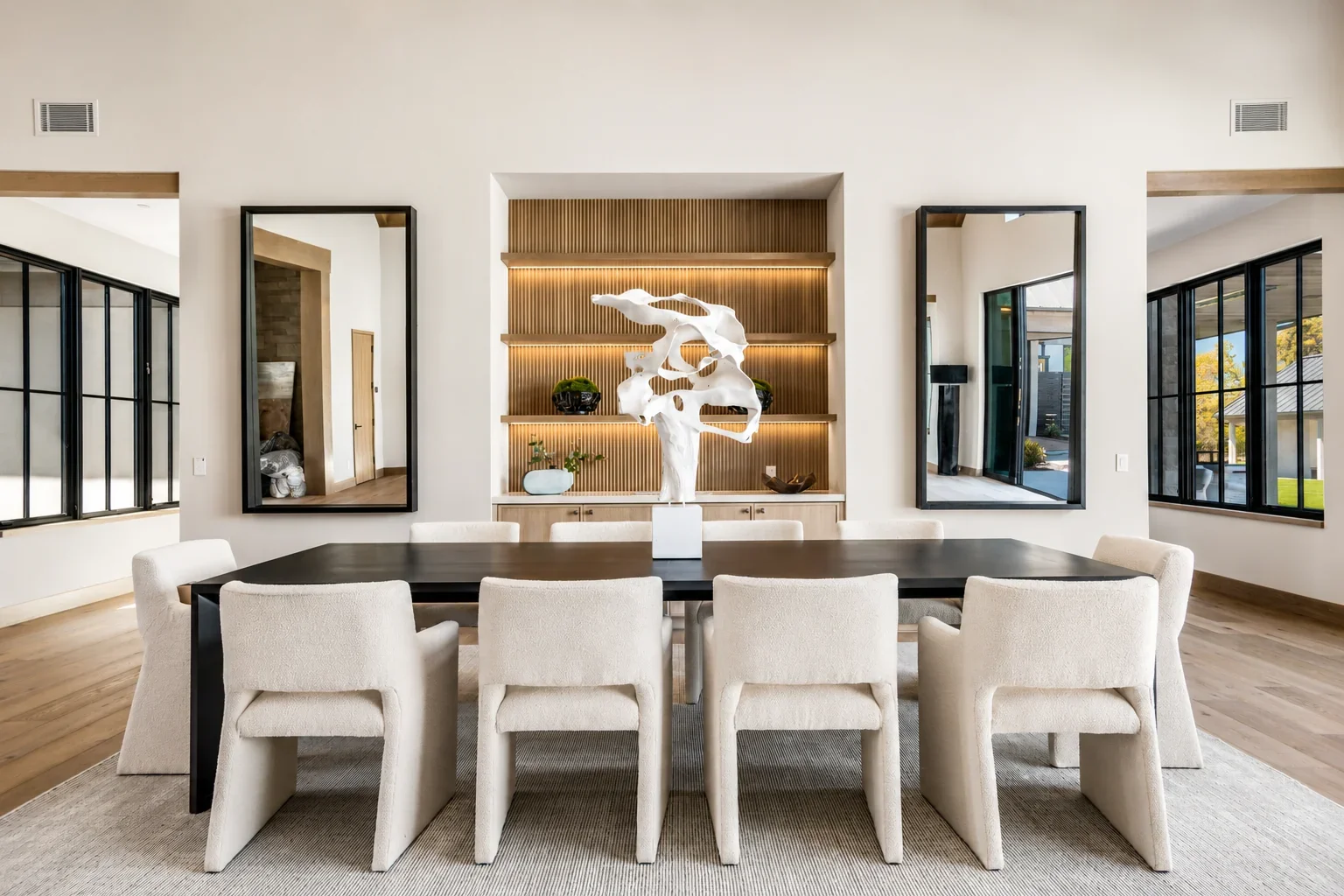 Interior of Trubody Ranch in Napa Valley featuring a dark dining table, upholstered seating, custom millwork, sculptural decor, and views to the landscaped exterior.