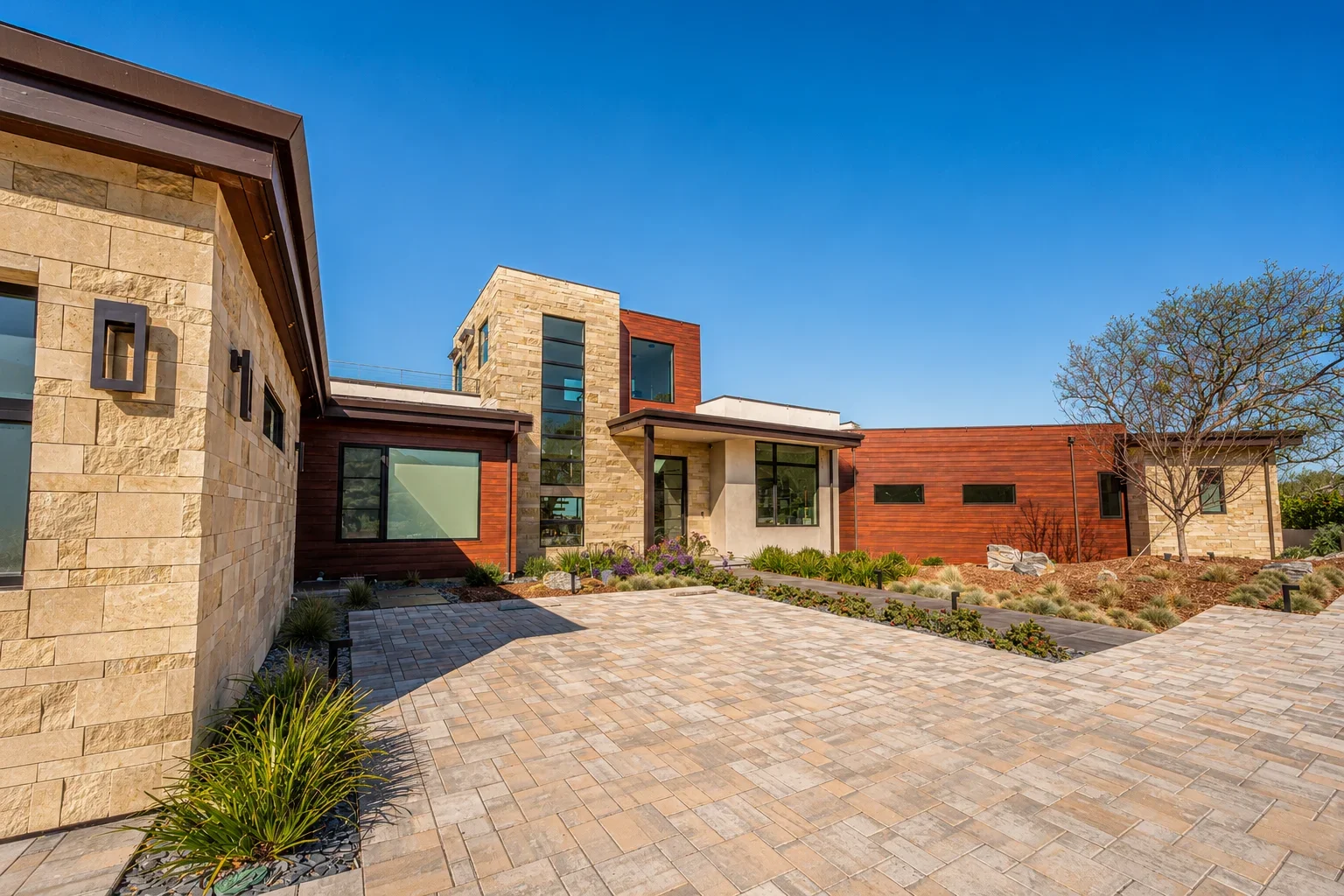 Front exterior of Gumtree in Los Gatos, featuring the modern custom residence with stone and wood cladding, expansive windows, a paved drive, and landscaped grounds.