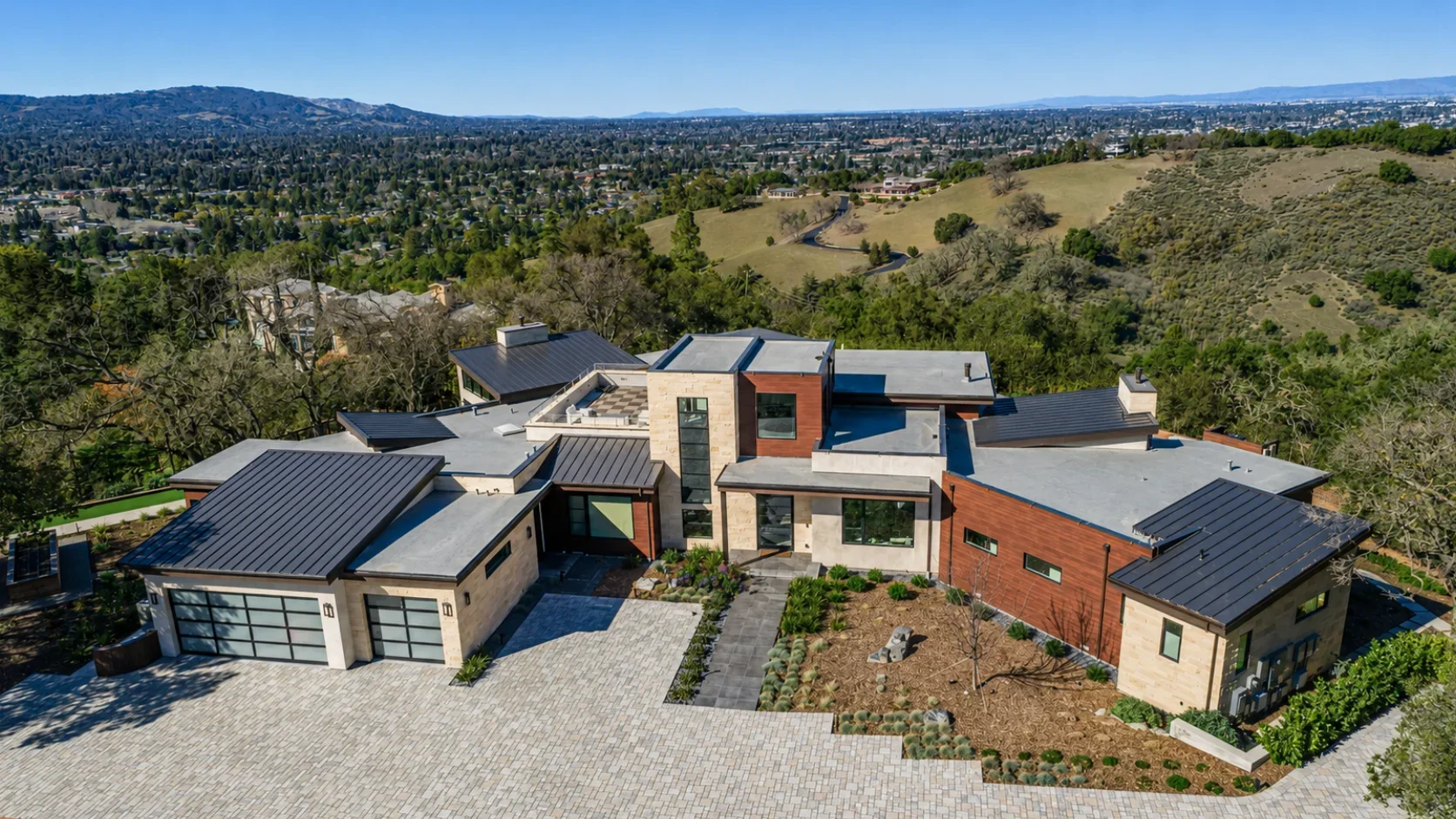 Hillside view of Gumtree in Los Gatos, featuring the modern custom residence with stone and wood cladding, a metal roof, landscaped grounds, and sweeping valley views.