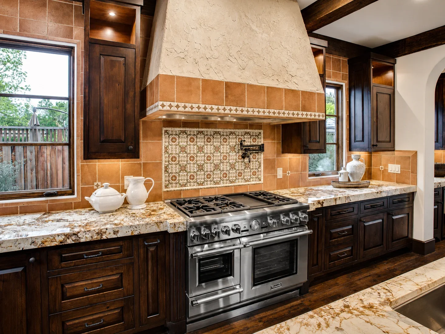 Kitchen at Villa Englewood in Los Gatos featuring dark wood cabinetry, granite countertops, a stainless steel range and hood, natural light, and decorative pottery.