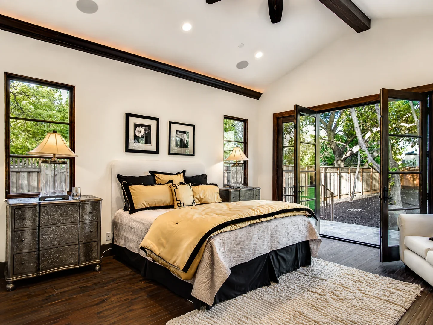 Bedroom at Villa Englewood in Los Gatos featuring layered gold and black bedding, metallic bedside tables, expansive windows, and glass doors opening to the garden.