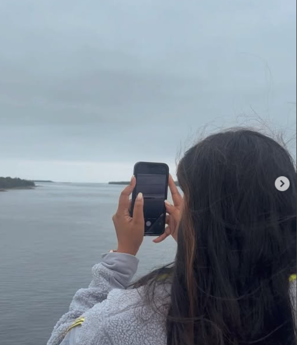 Person taking a photo with a smartphone overlooking a body of water on an overcast day.