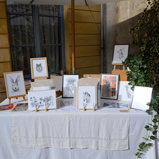 Table d'exposition avec des dessins animaliers sur des chevalets, incluant un hibou, un lapin, un cerf et un cheval.
