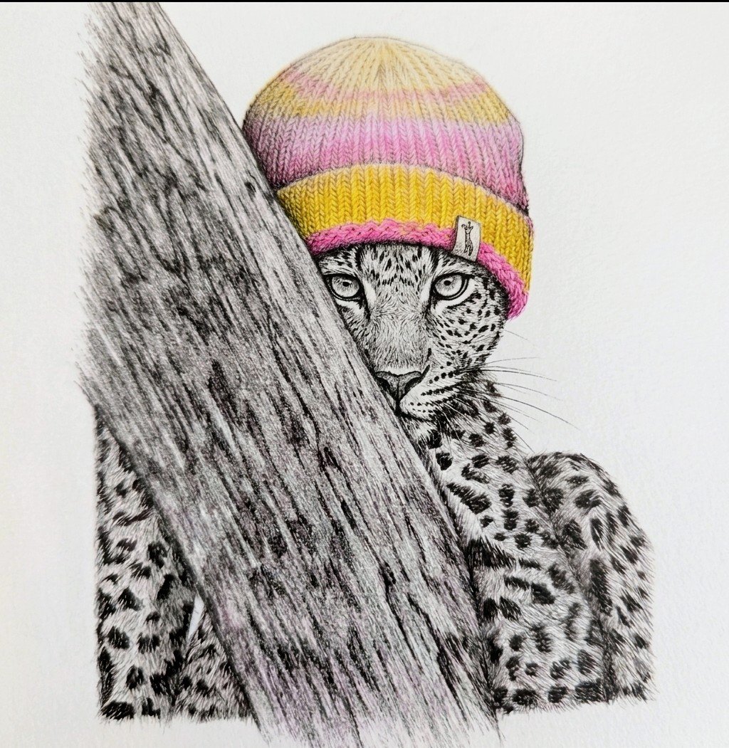 Un dessin en noir et blanc d'un léopard avec un bonnet coloré rose, jaune, et beige, cachant partiellement son visage derrière un arbre, avec un fond blanc.