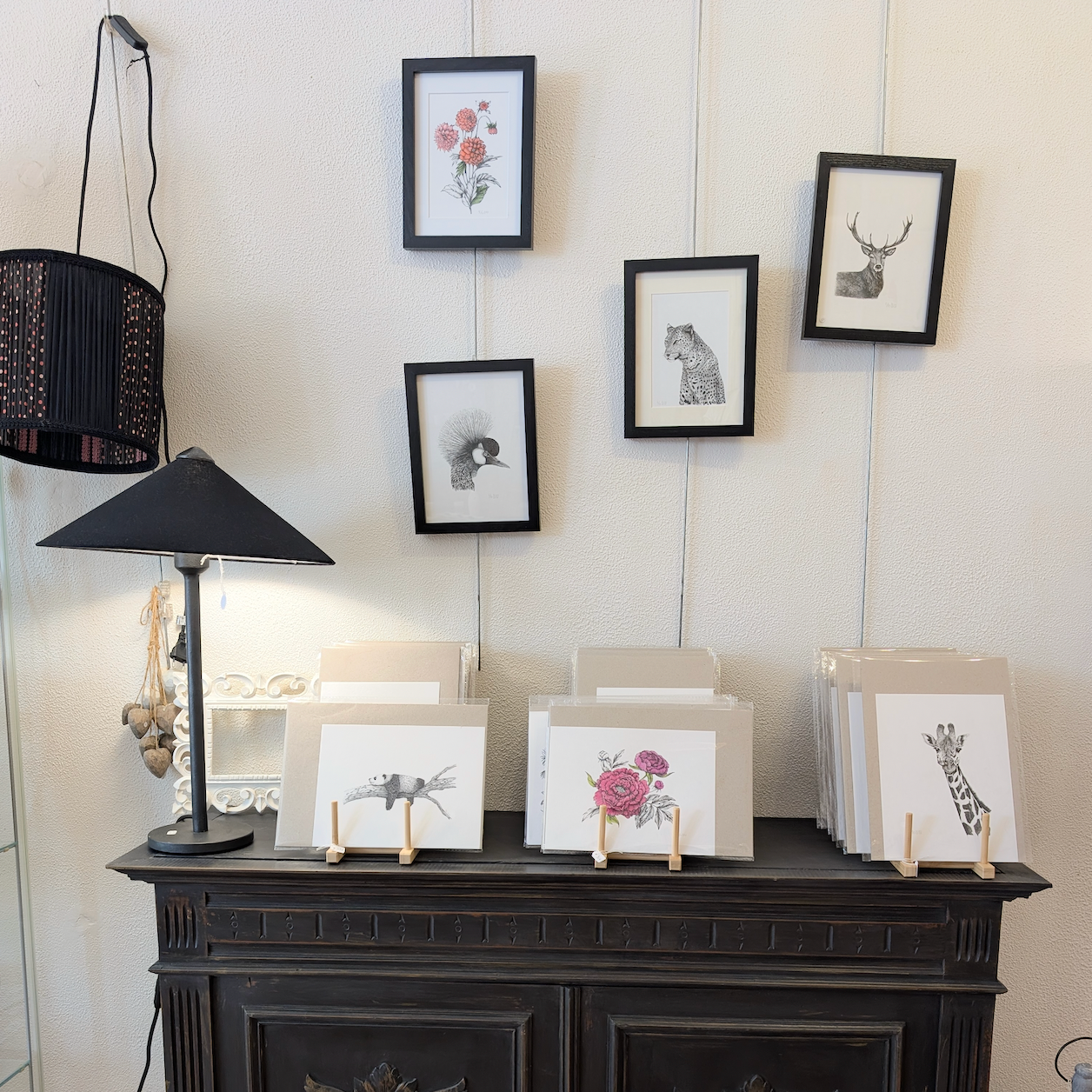 Une vitrine avec des dessins fait main, avec patience et minutie, d'animaux tels qu'une grue, une girafe, un léopard, et un cerf, exposés dans une boutique d'artisanat. Fleurs colorées à l'aquarelle.