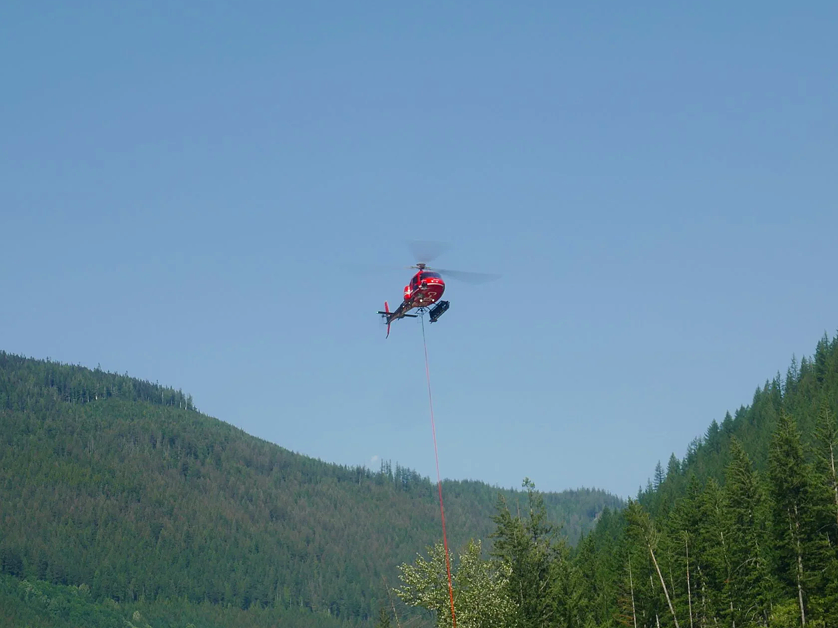Aerial footage of a helicopter operating over a forested mountain landscape in British Columbia