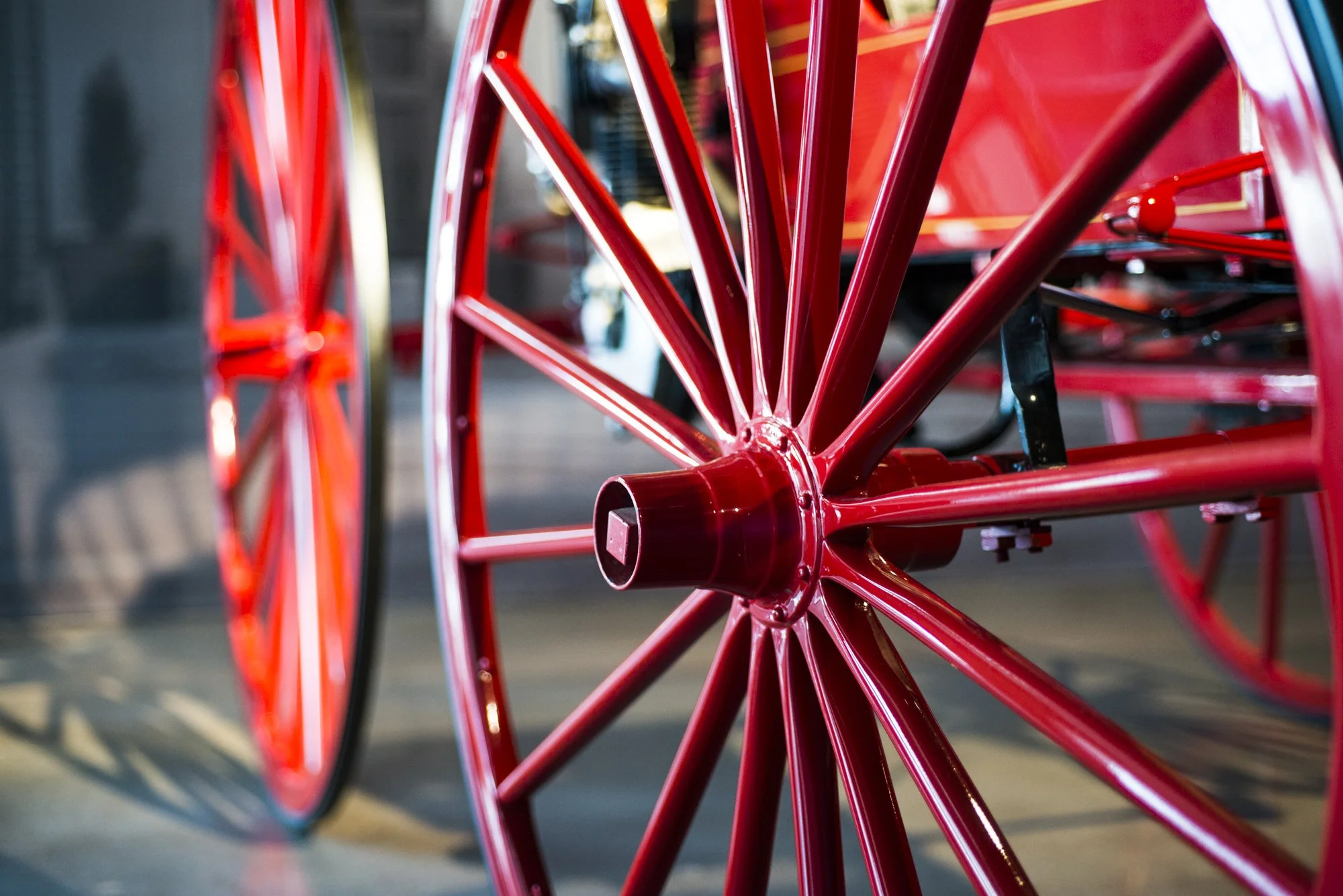 Close-up of a red wheel and spokes of a vintage-style rickshaw or carriage with a blurred background.