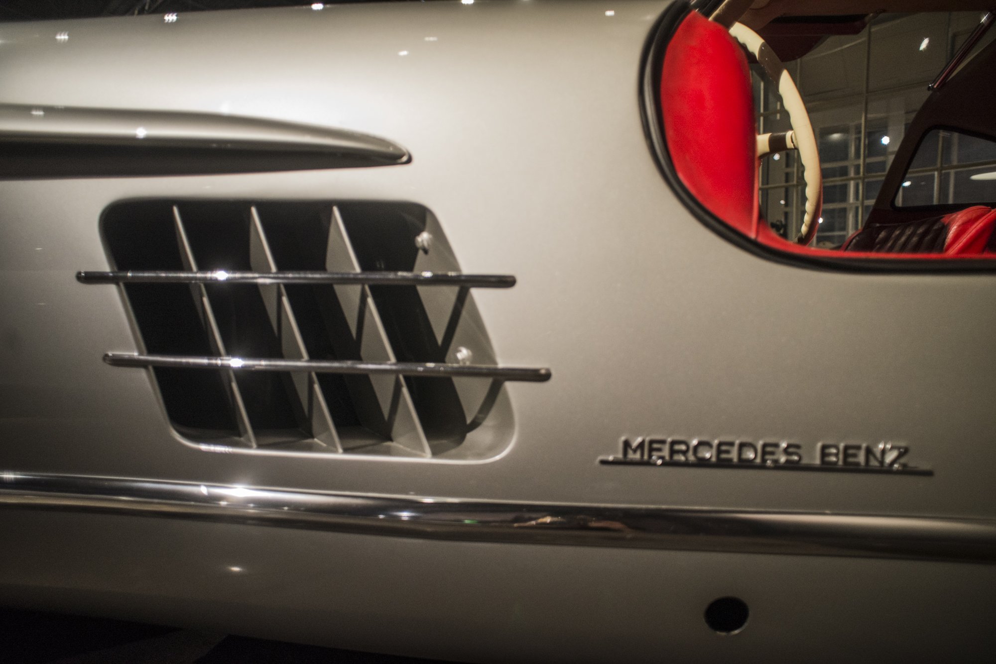 Close-up of a silver Mercedes-Benz car's front grille and part of the interior with red upholstery visible through the open window.
