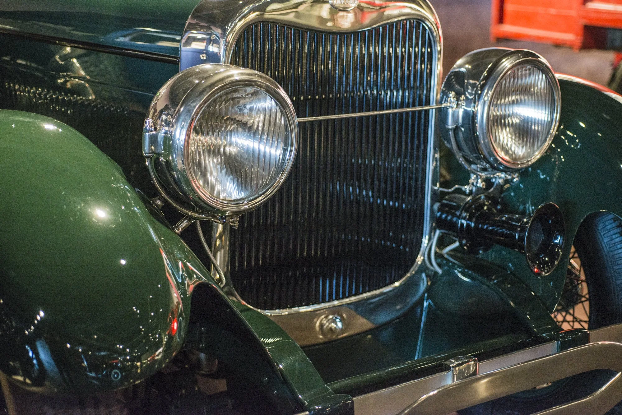 Close-up of vintage car headlights, grille, and front fender, showing chrome details and deep green paint.