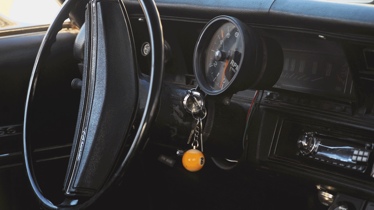 Close-up of a vintage car dashboard with a tachometer, car keys with a yellow 8-ball keychain, and a stereo system.
