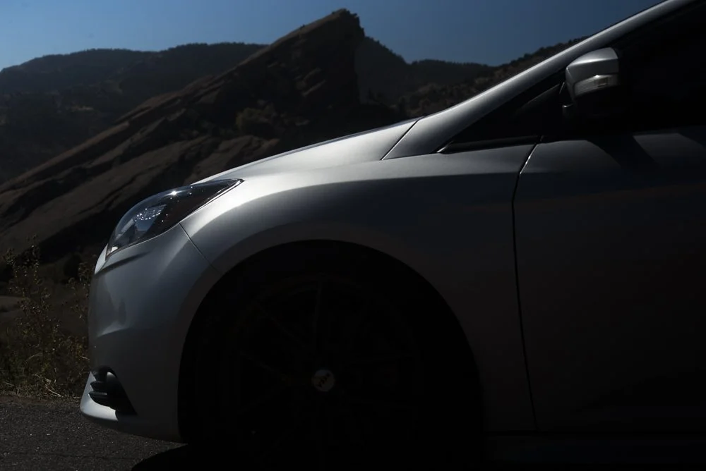 Close-up of a modern silver car parked outdoors with mountains in the background, under a blue sky.