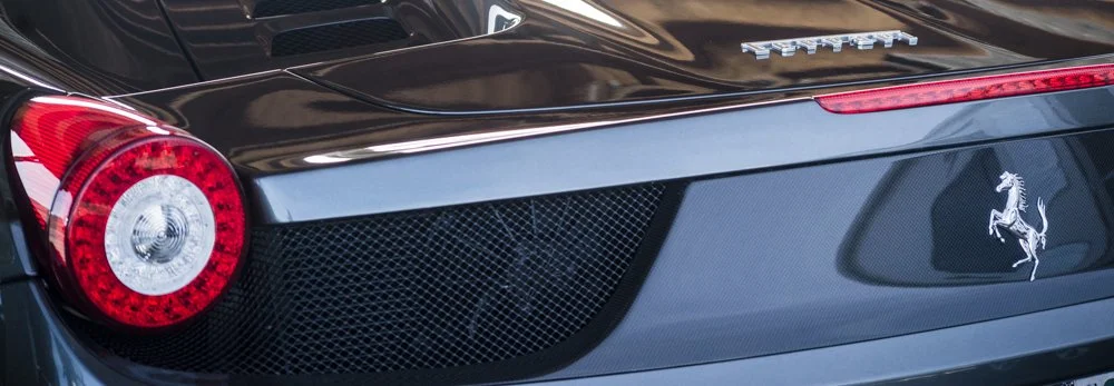 Close-up of the rear of a black Ferrari sports car, showing tail lights, rear grille, and the Ferrari logo.