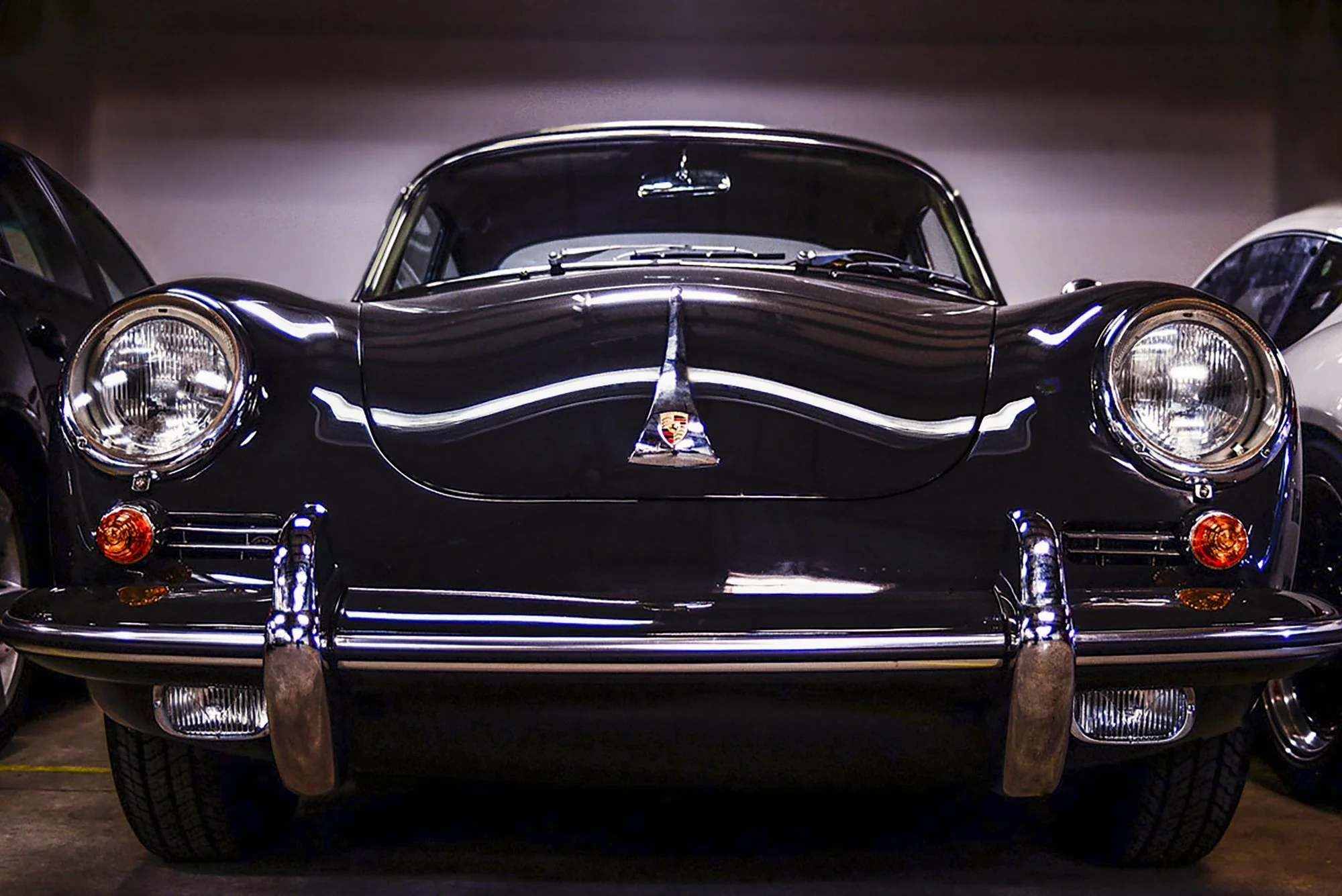 Front view of a vintage black Porsche sports car with a shiny exterior, large round headlights, and chrome accents, parked between two other cars.